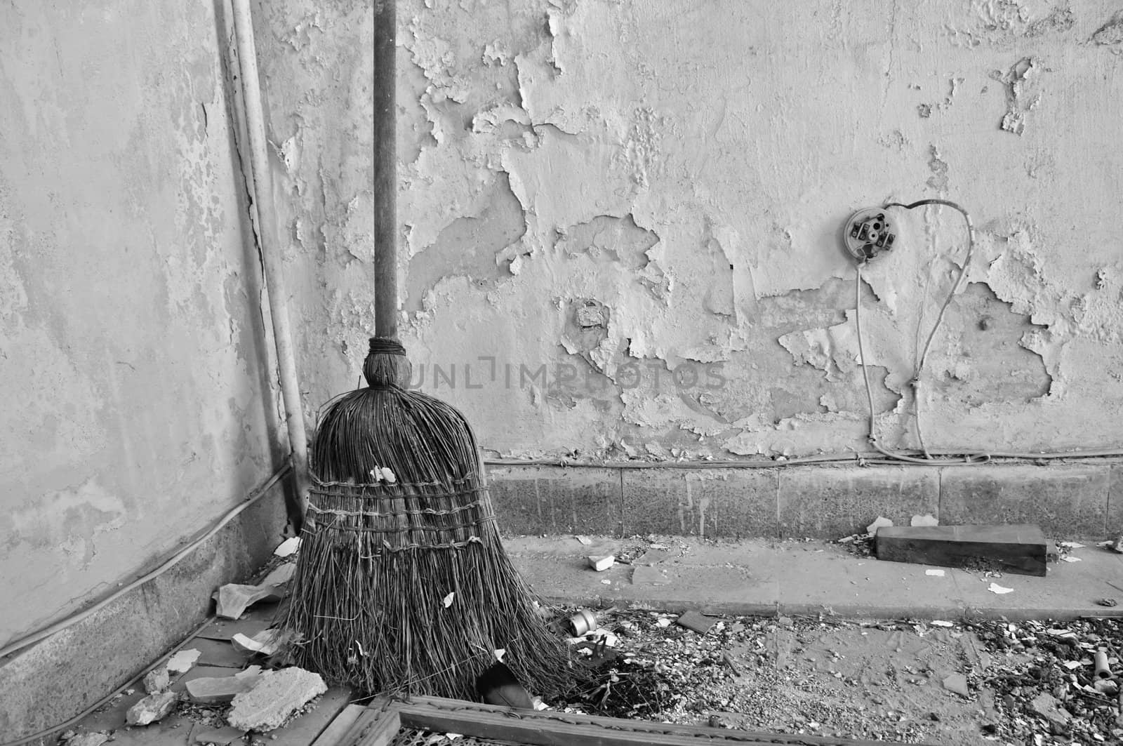 Dusty straw broom on filthy floor of abandoned house. Black and white.