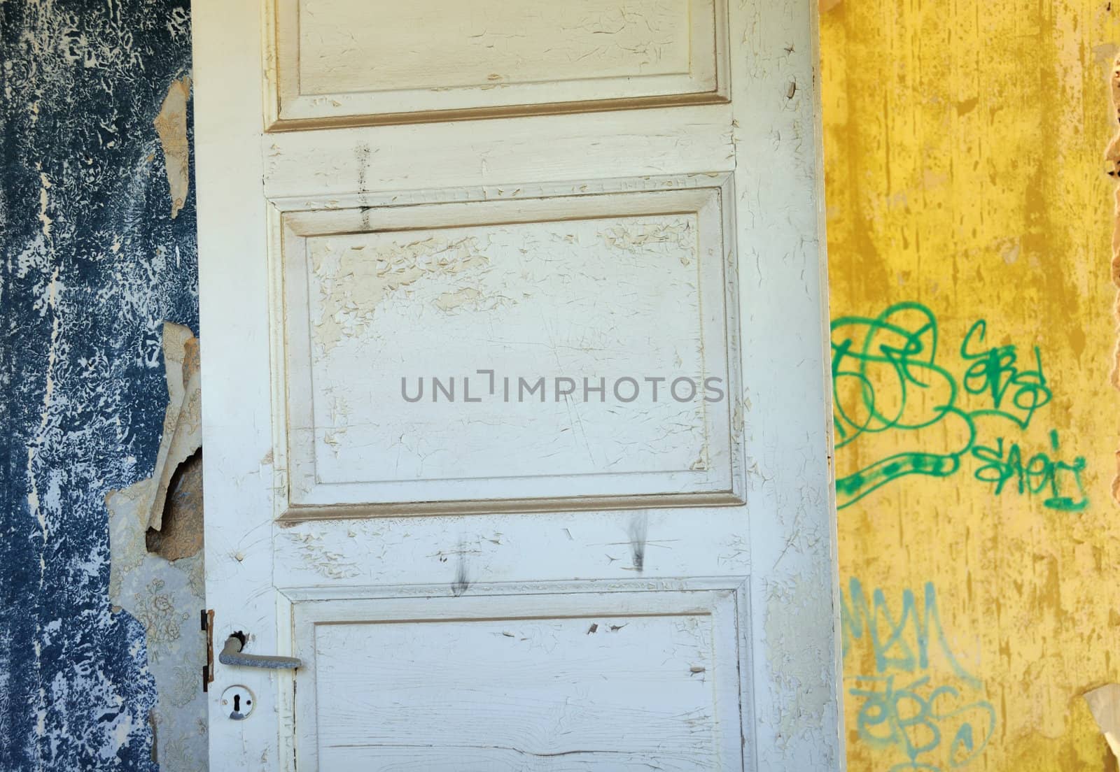 Wooden door, torn vintage wallpaper and peeling walls in abandoned interior.