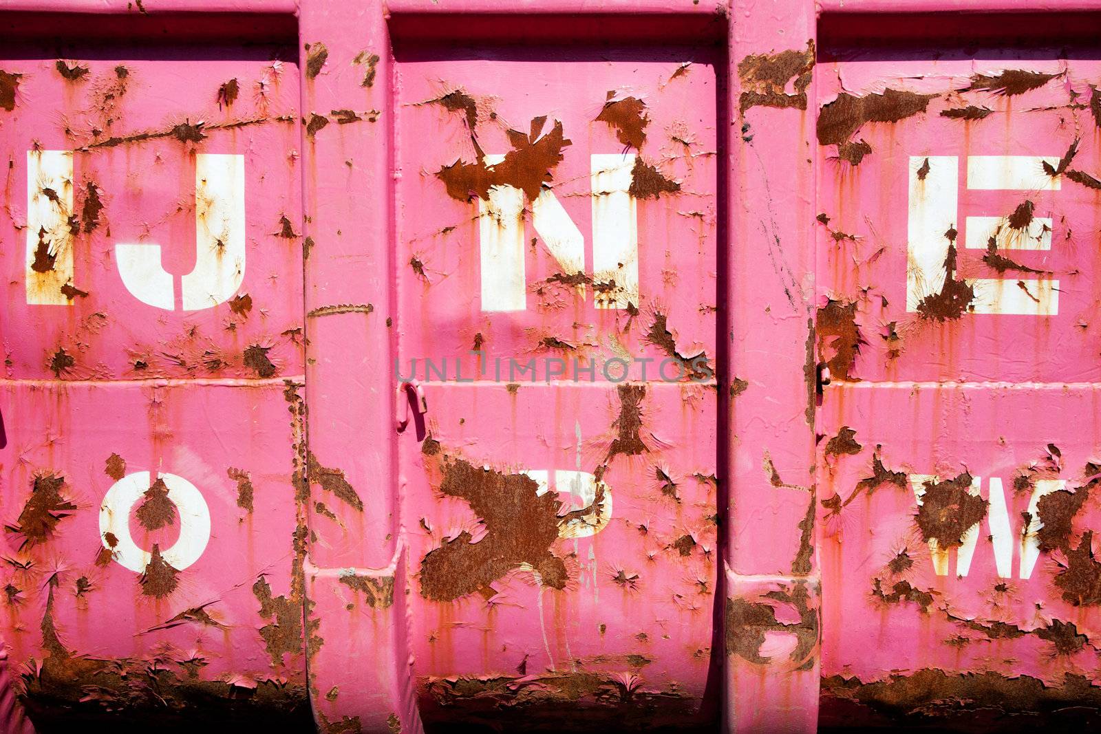 rust and peeling pink paint with letters on metal surface of lorry