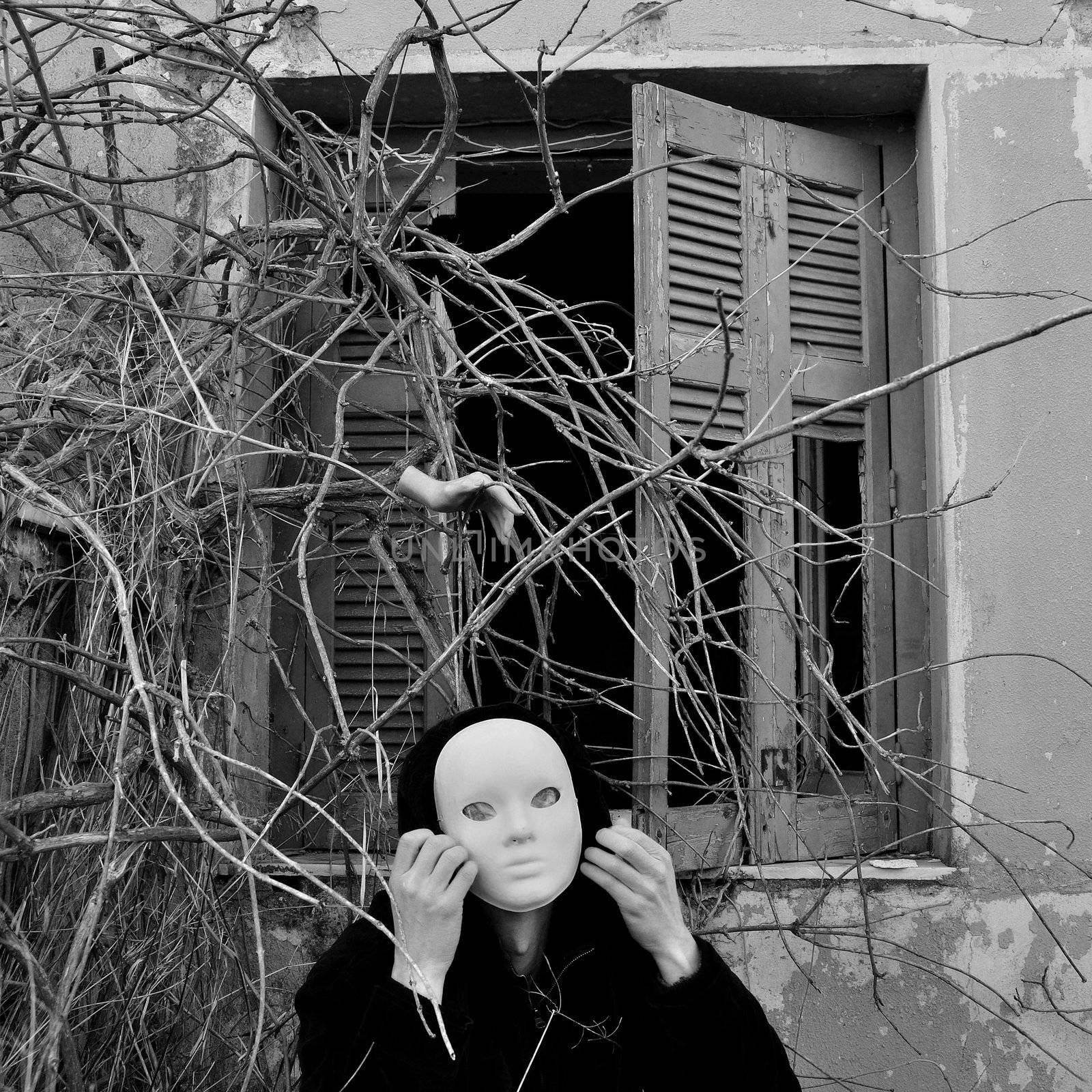Figure with white mask under window with overgrown plants and doll hand. Black and white.