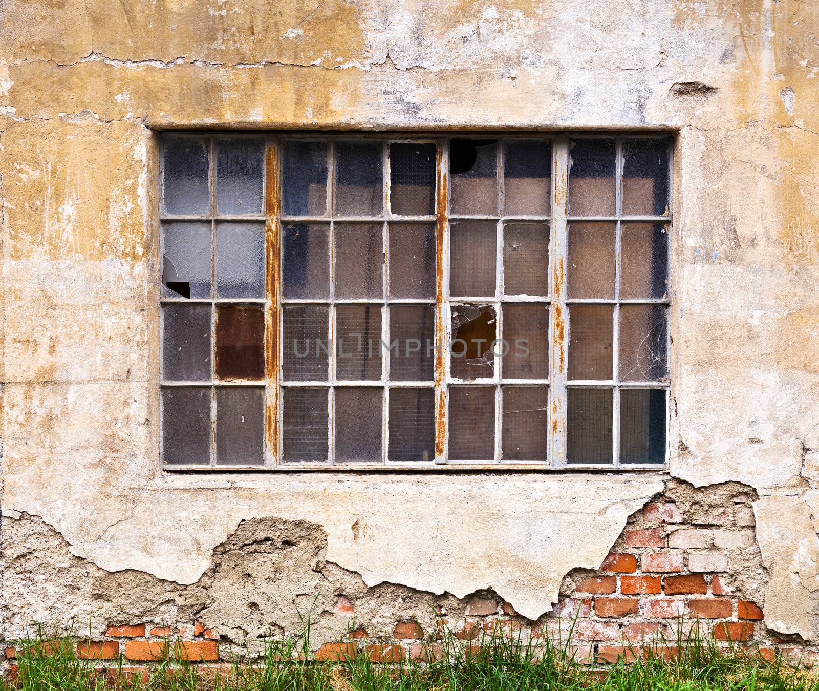 A large window with broken panes on the wall of a dilapidated old building