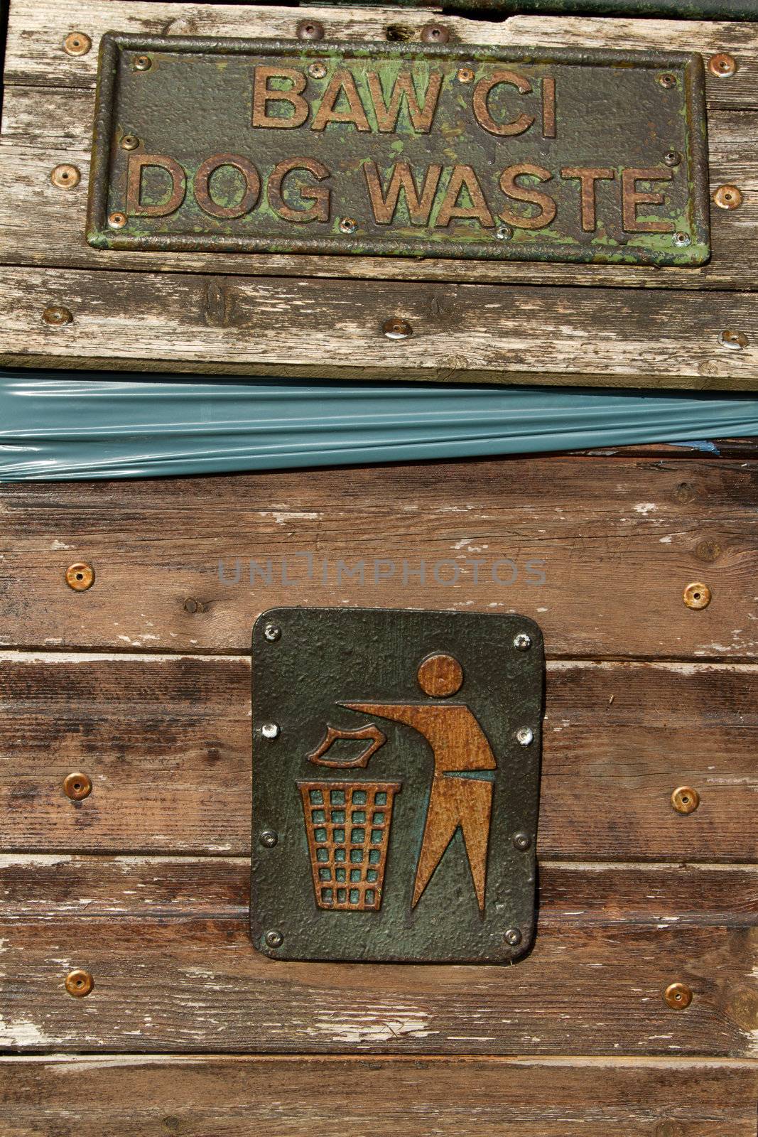A pair of metal signs on a wooden bin showing a figure putting litter in a bin and the words 'DOG WASTE'.