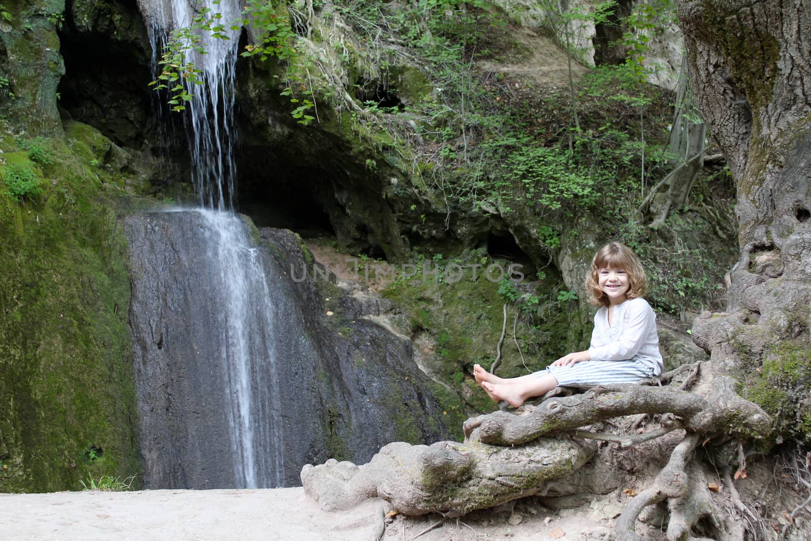 little girl sitting next to a waterfall