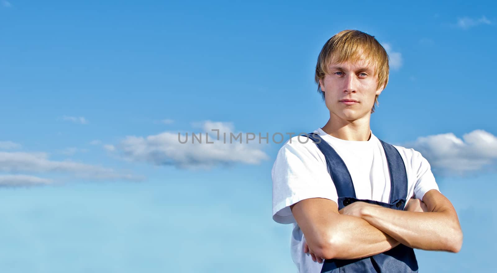 Handsome handyman in coveralls on sky background