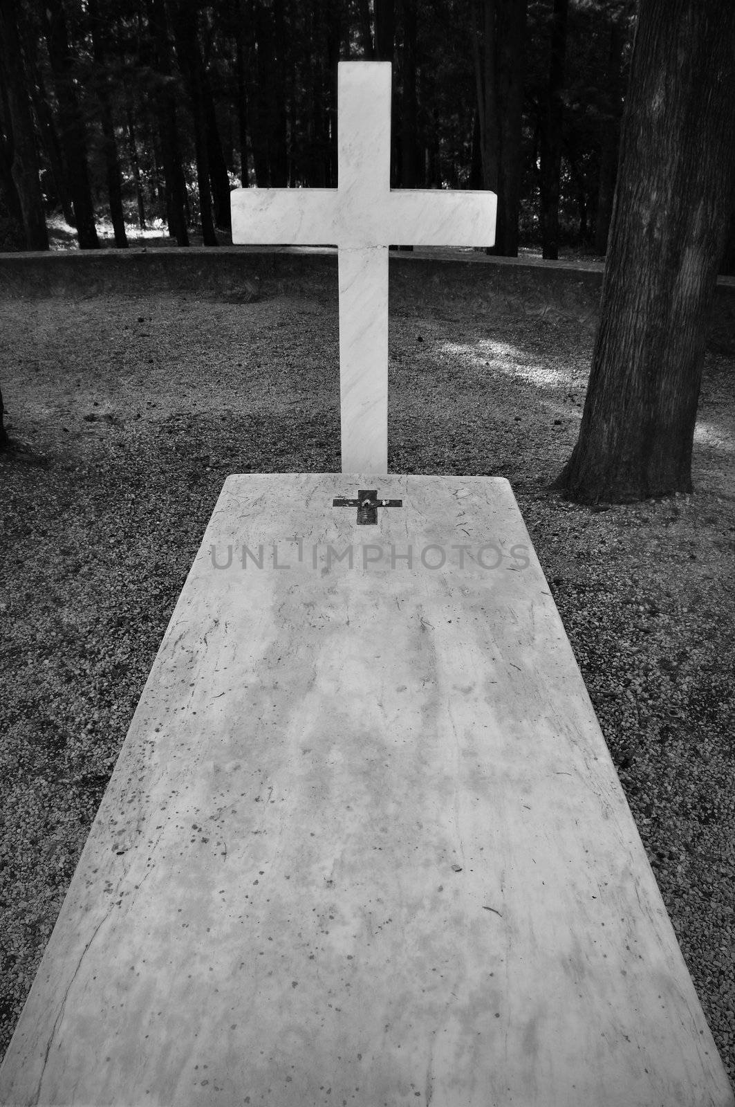 Cross and marble grave tombstone among trees.