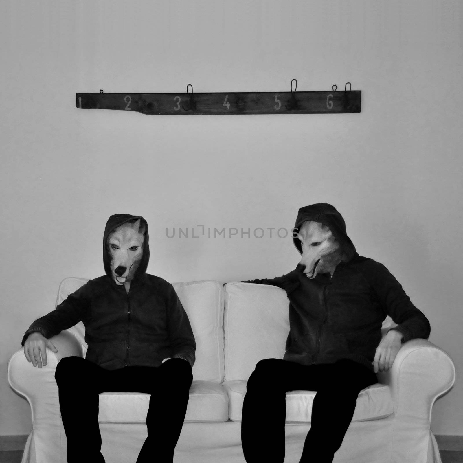 Two figures with dog mask sitting on couch. Black and white.