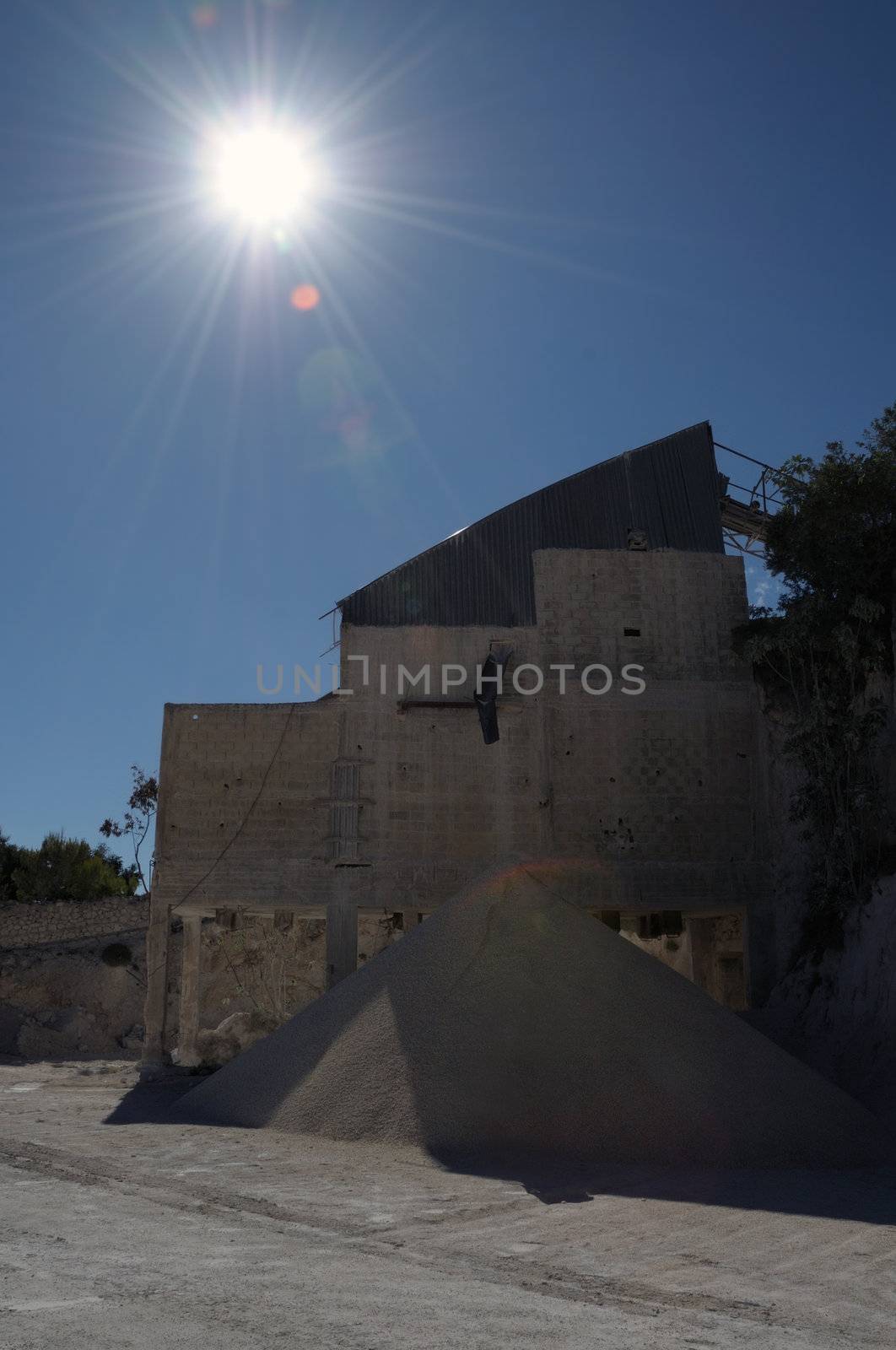 Industrial building and pile of gravel at mining and quarry site. Midday sun lens flare.