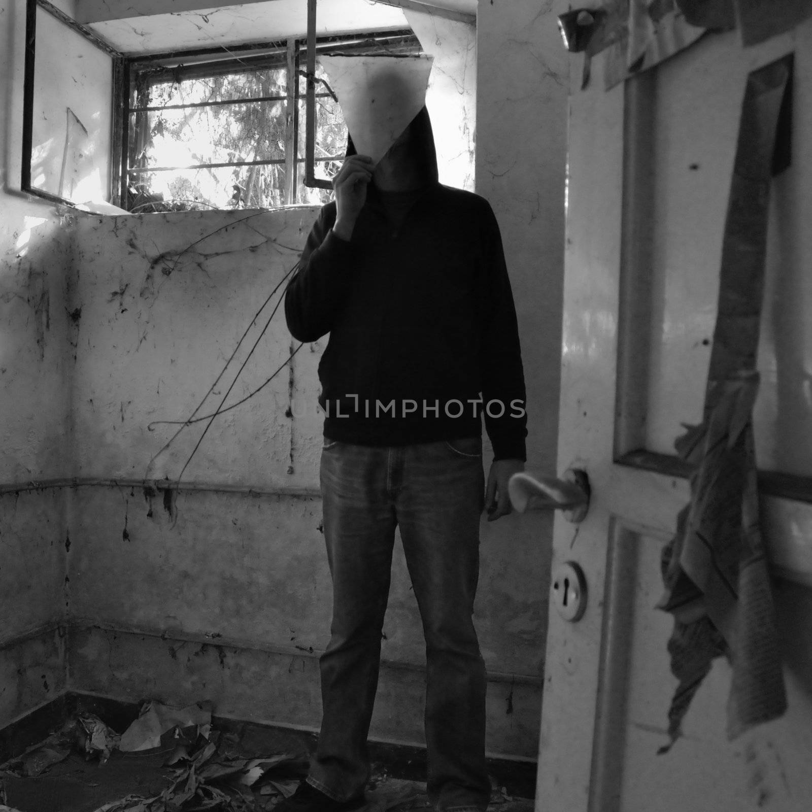 Hooded man obscured by piece of broken glass in decayed dirty room.