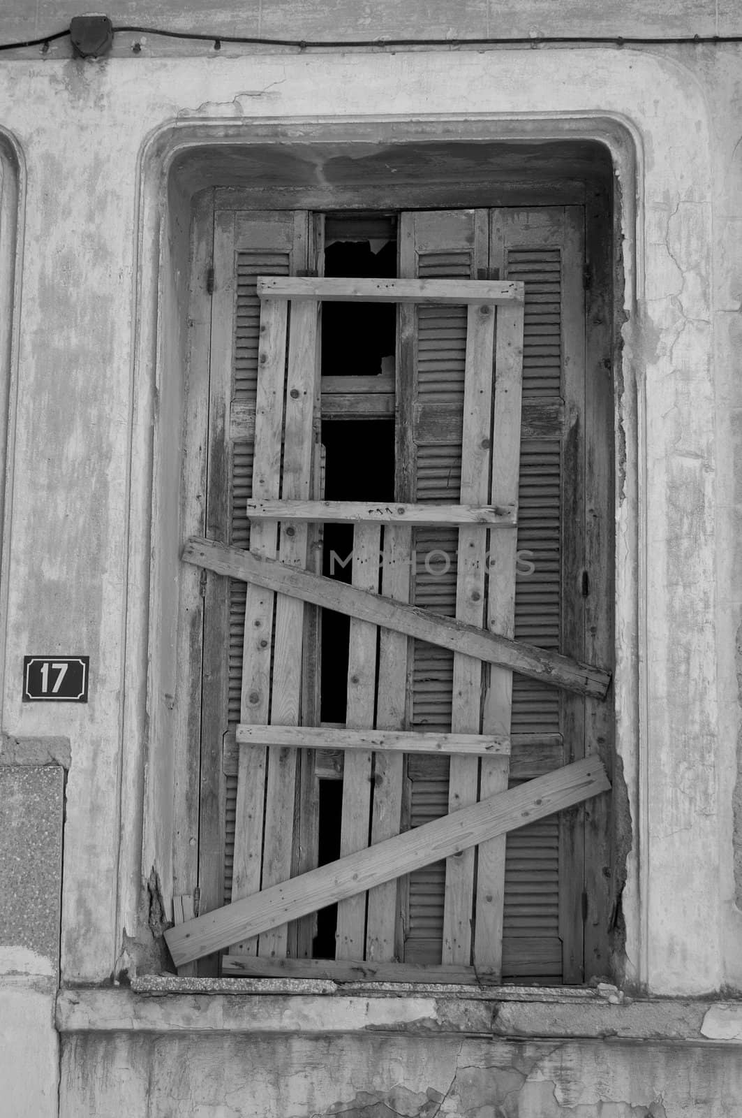 Broken window shutter sealed with planks and weathered wall of abandoned building.