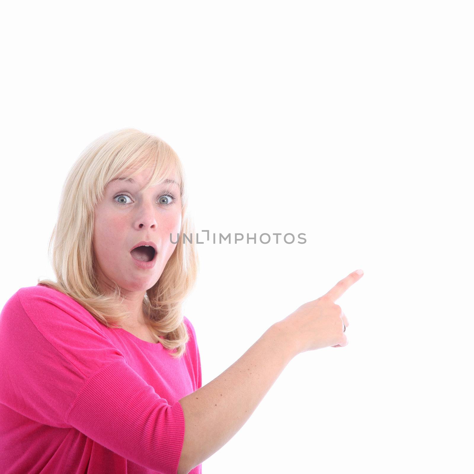 Awestruck woman pointing to blank copyspace with her finger as she looks at the camera in open mouthed astonishment 