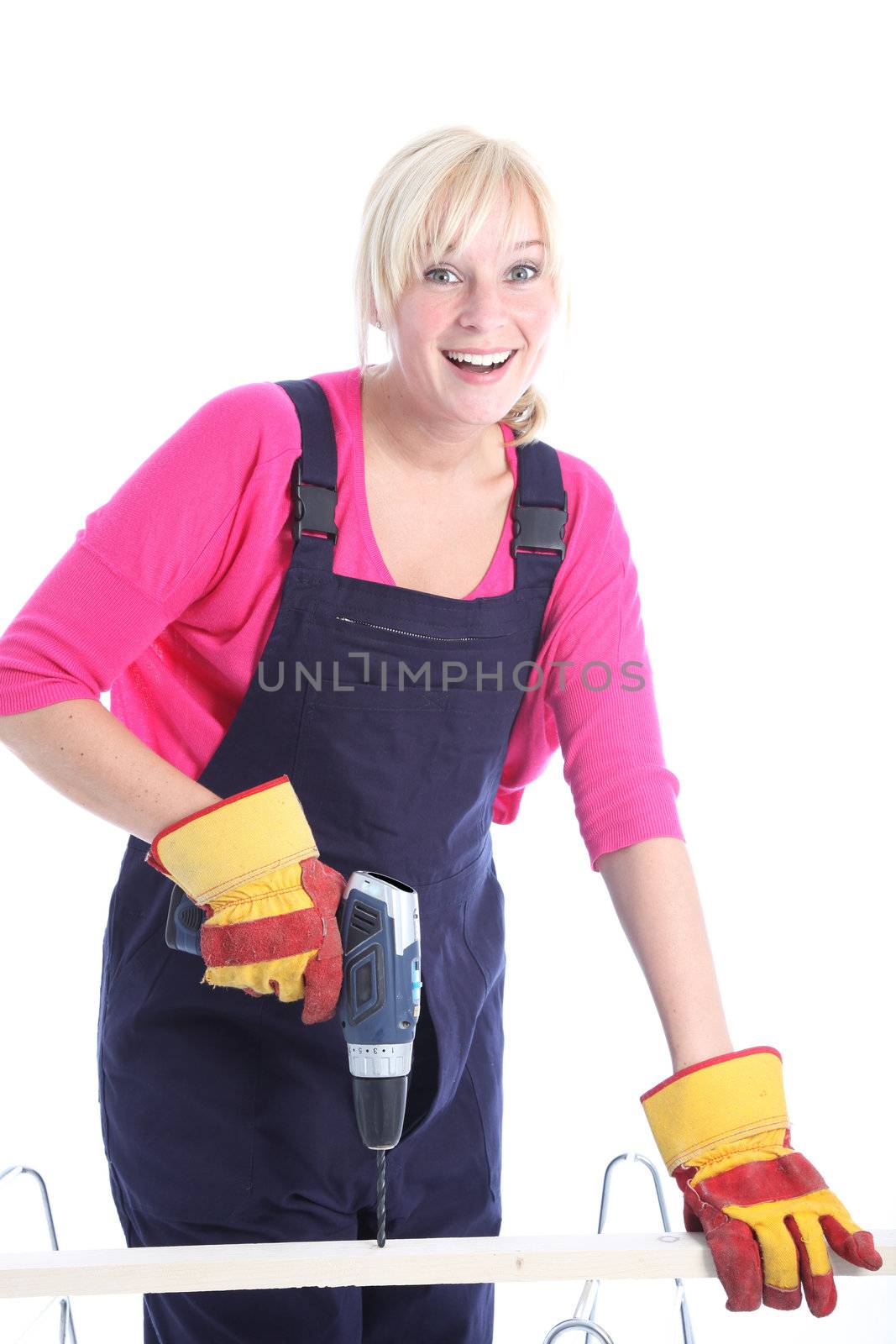 Happy woman in dungarees doing DIY renovations drilling a hole in a plank of wood isolated on white 