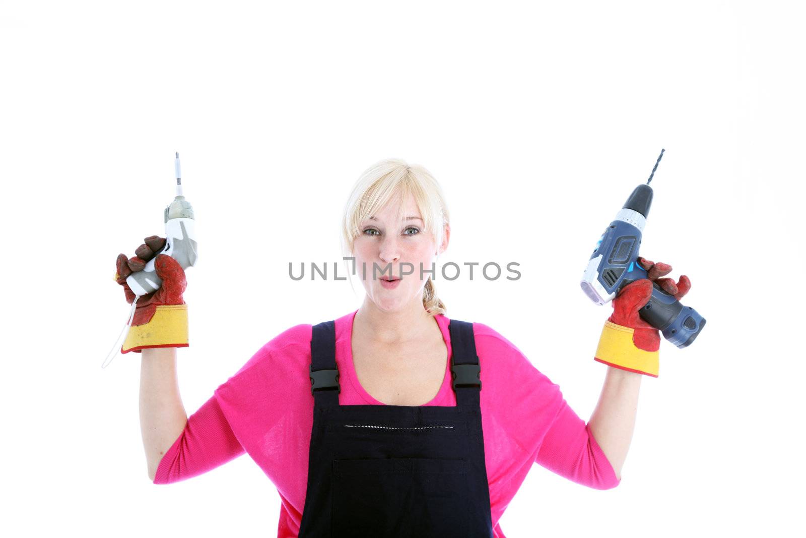 Laughing woman in dungarees holding up a mechanical screwdriver and portable handheld drill isolated on white 