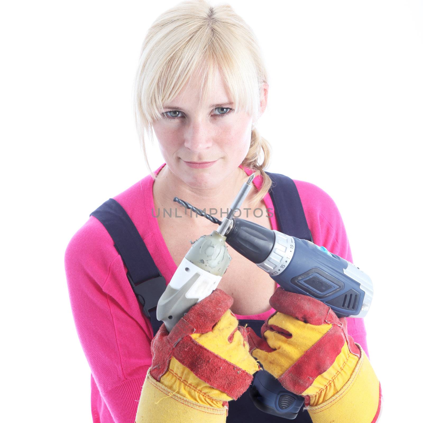 Woman DIY in dungarees and protective gloves holding a screwdriver and portable drill in front of her with a determined expression Woman DIY in dungarees and protective gloves holding a screwdriver and portable drill in front og her with a determined expression 