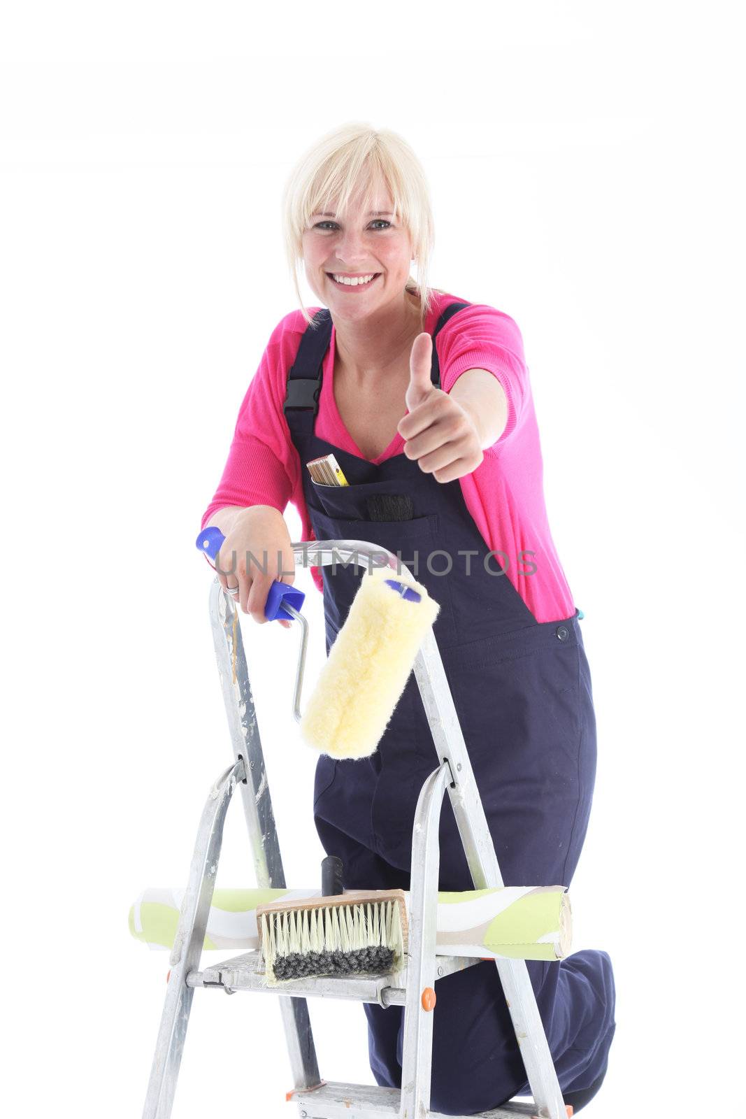 Enthusiastic female decorator on a ladder giving a thumbs up gesture of approval and success for her DIY wallpapering project, isolated on white