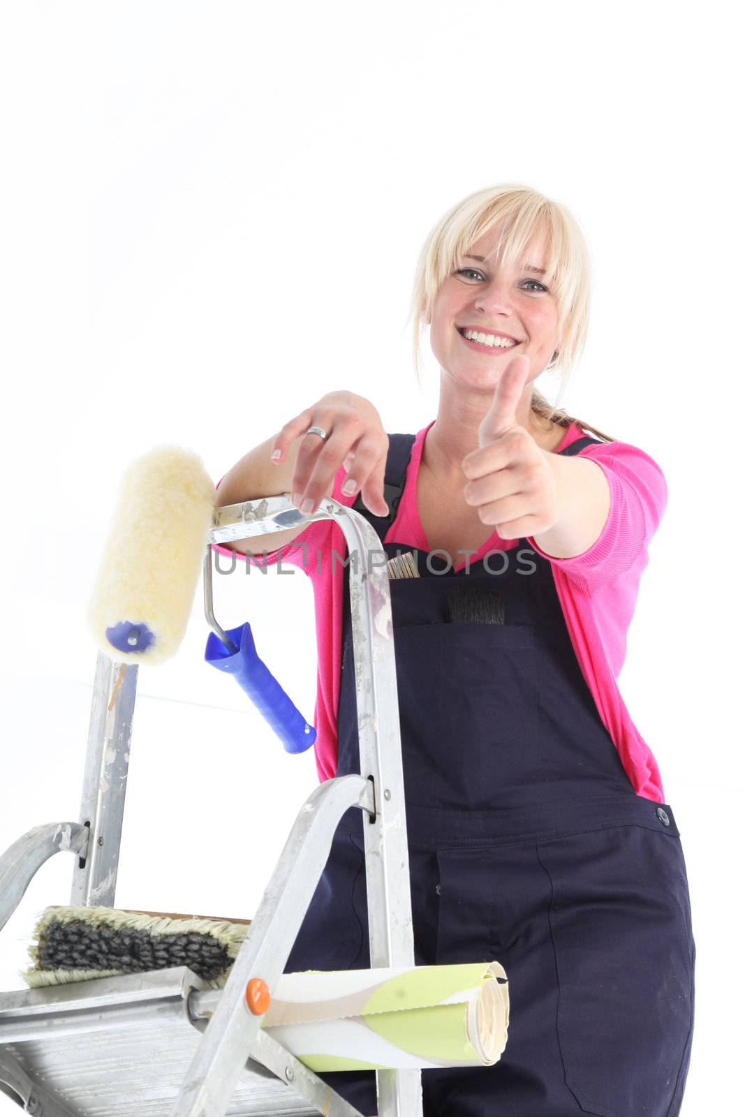 Happy positive housewife wallpapering looking down from the top of her ladder giving a thumbs up gesture 