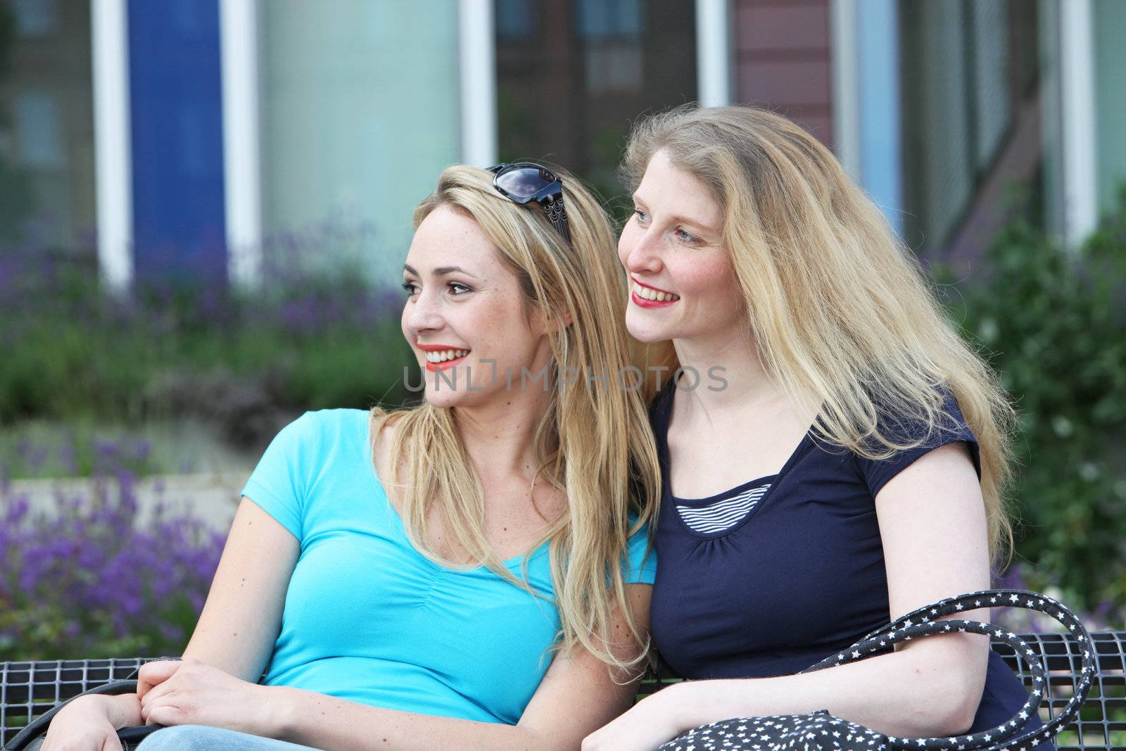 Happy women sitting close together on a bench in the sunshine both looking in the same direction off screen Happy women sitting close together on a bench in the sunshine both looking in the same direction of screen