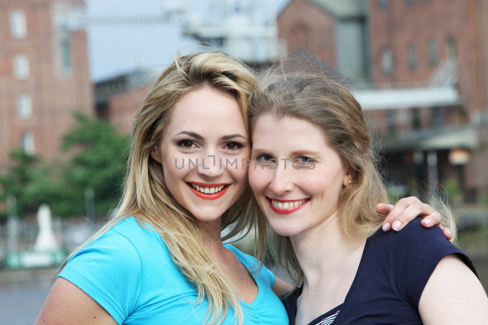 Smiling happy women standing with their heads close together in a display of friendship in an urban environment with buildings 