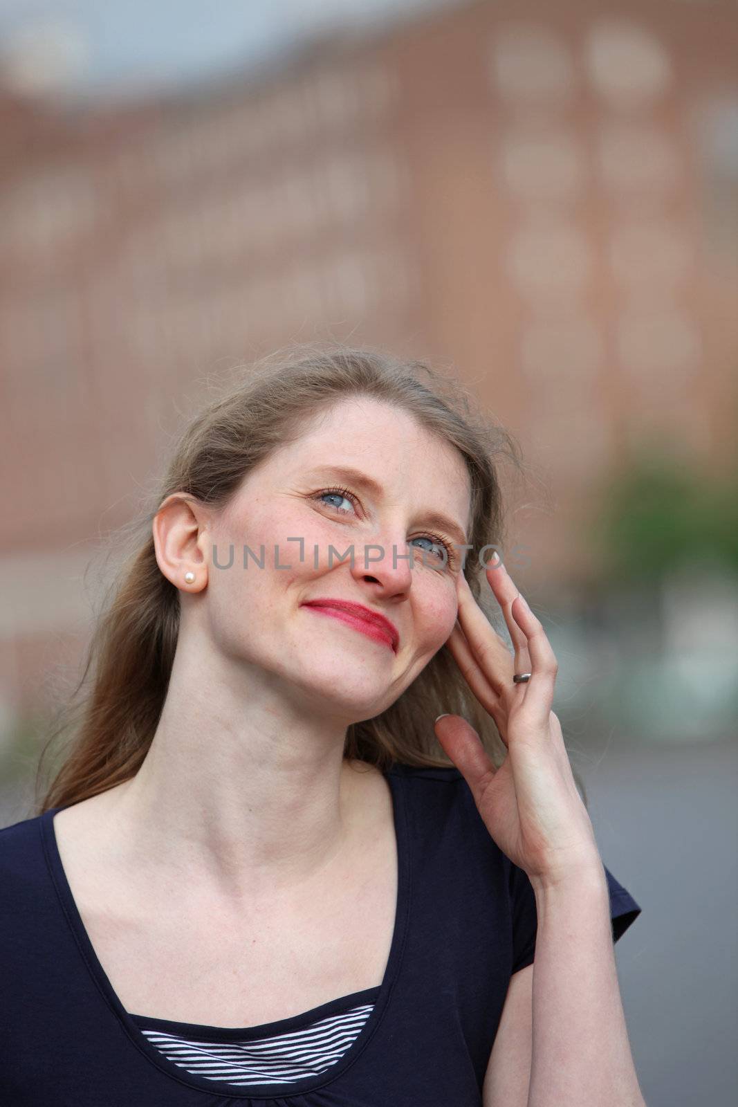 Smiling graceful woman with her fingertips to her temple and her eyes raised to the sky in an urban environment 