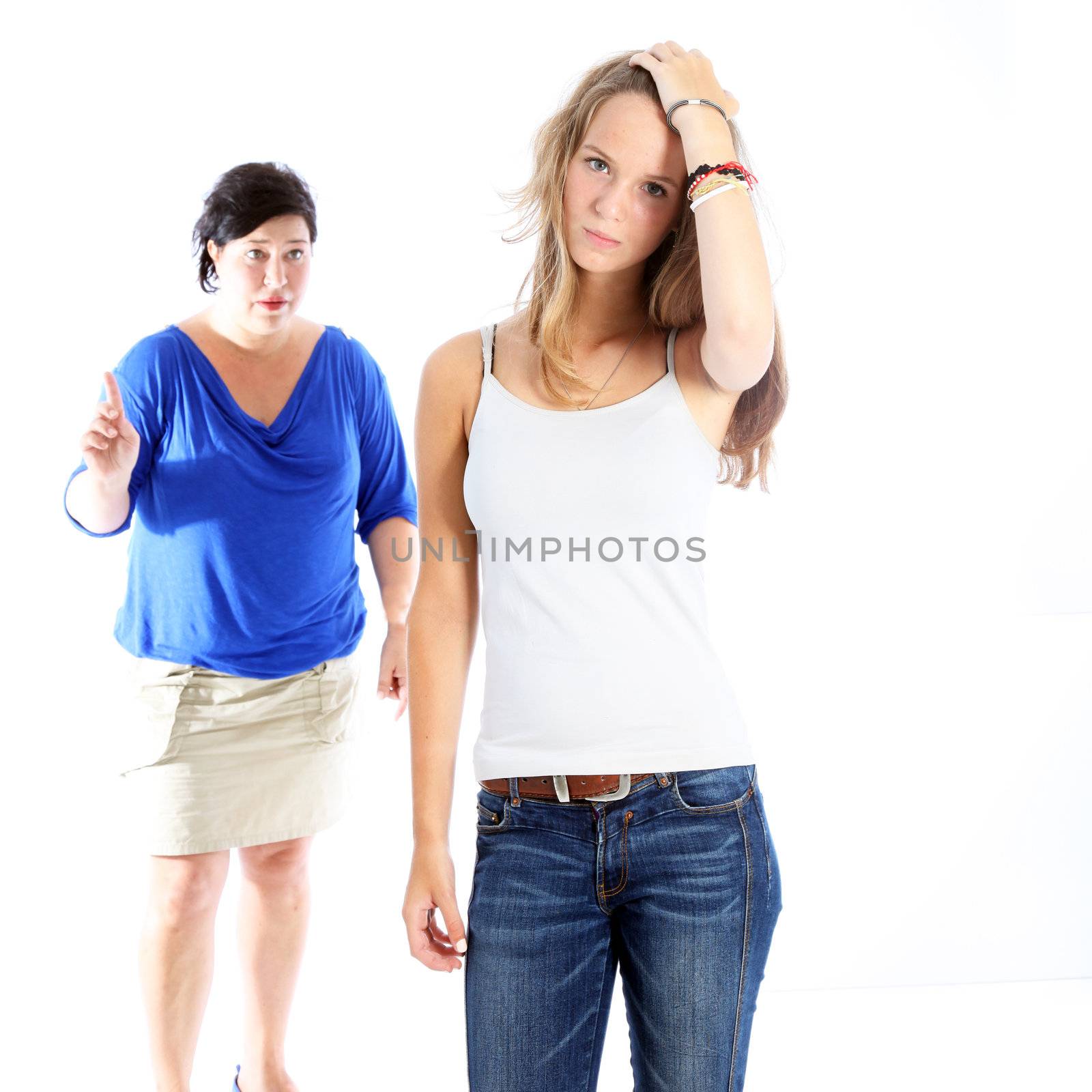 Mother admonishing her daughter who is standing with her hand to her head and a rebellious expression isolated on white Mother admonishing her daughter who is standing with her hand to her head and a rebellious expression isolated on white