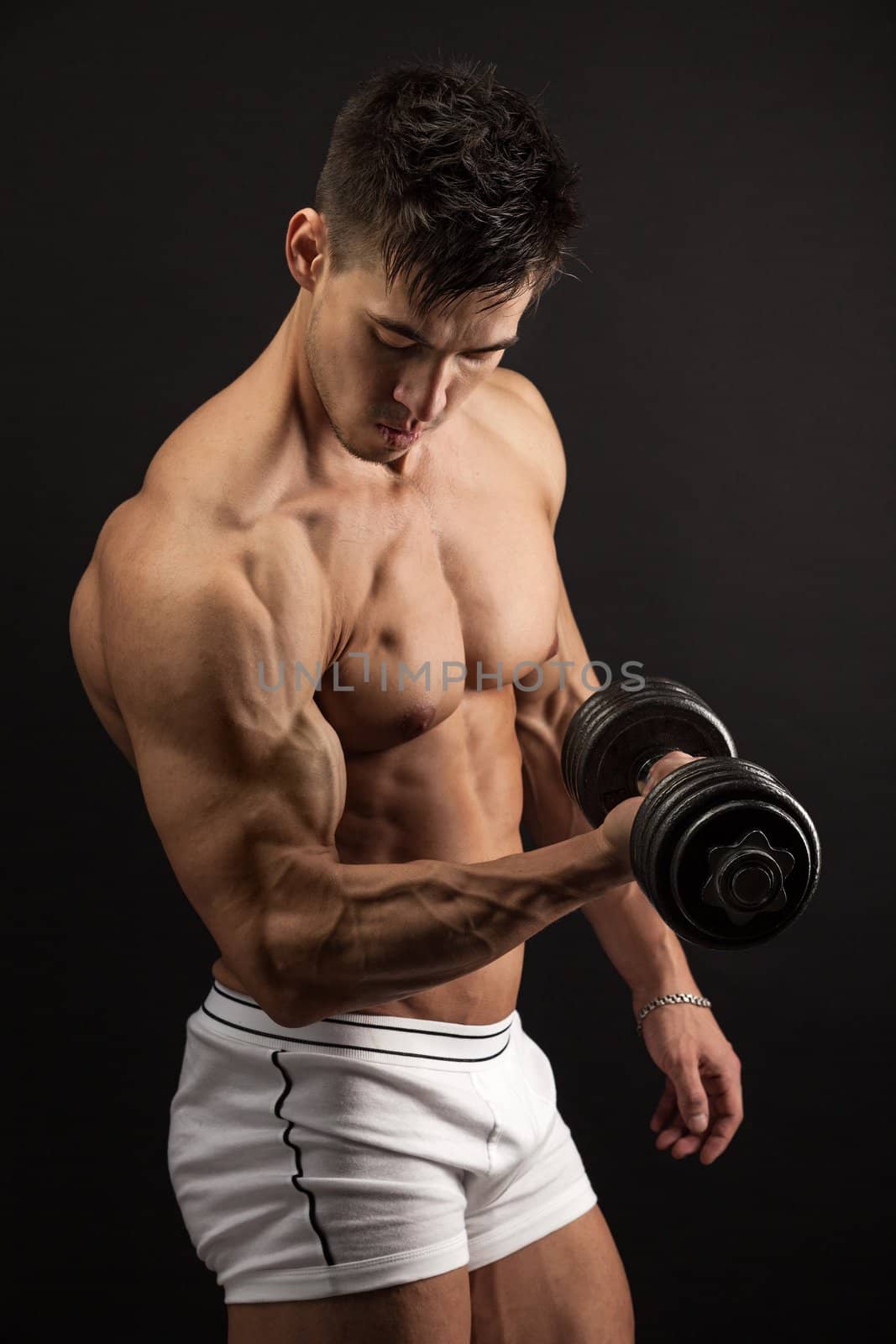 Muscular young man lifting a dumbbell over black background
