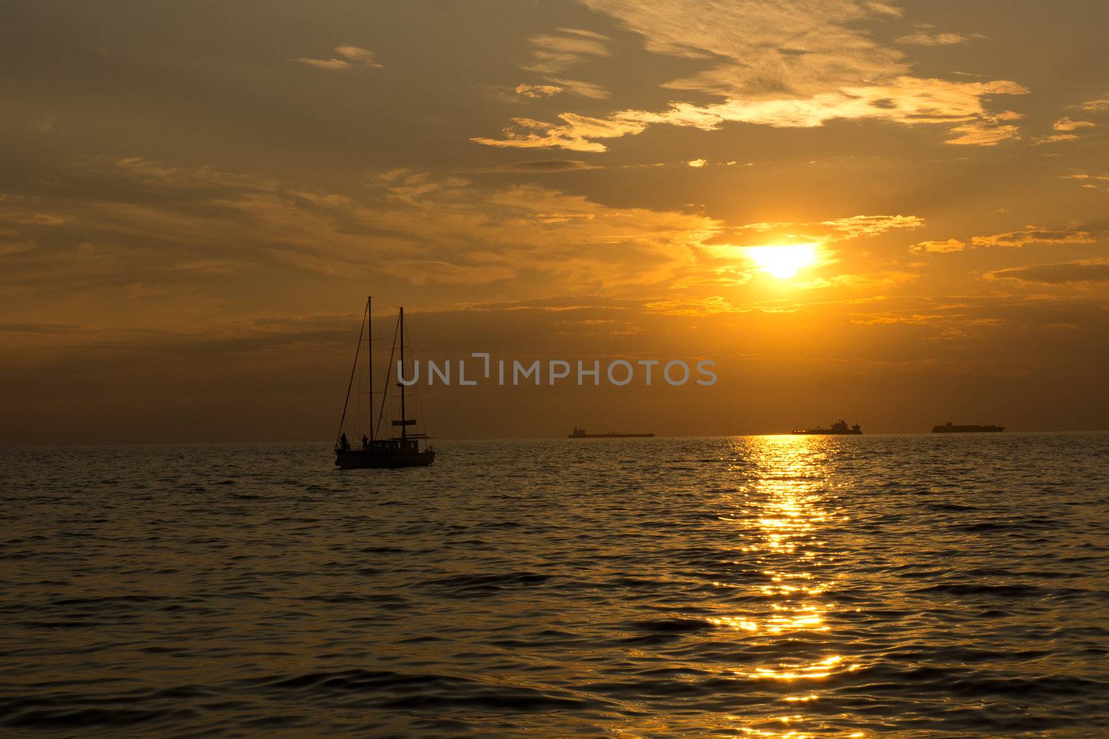 Sea ships and sailboats silhouettes against sunset.