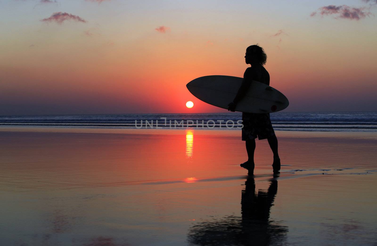 Silhouette of surfer at red sunset. Kuta beach. Bali