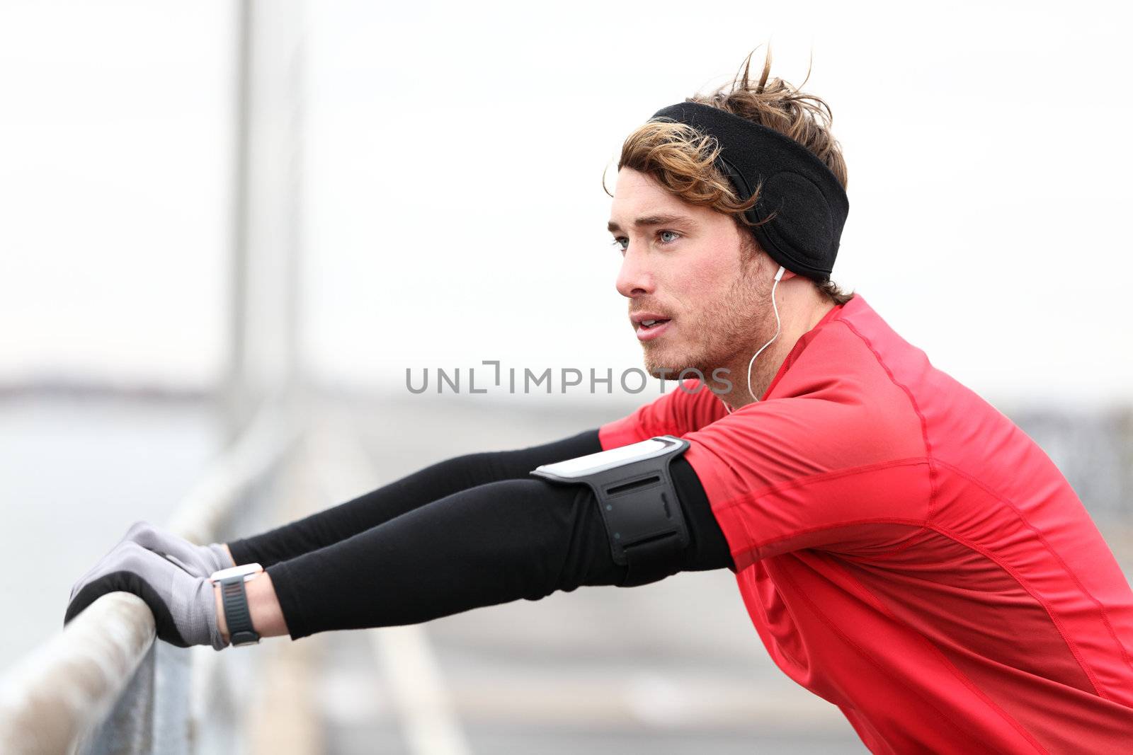 Male runner stretching after running in cold fall weather wearing warm sporty running clothing. Handsome male fitness sport model outdoors.