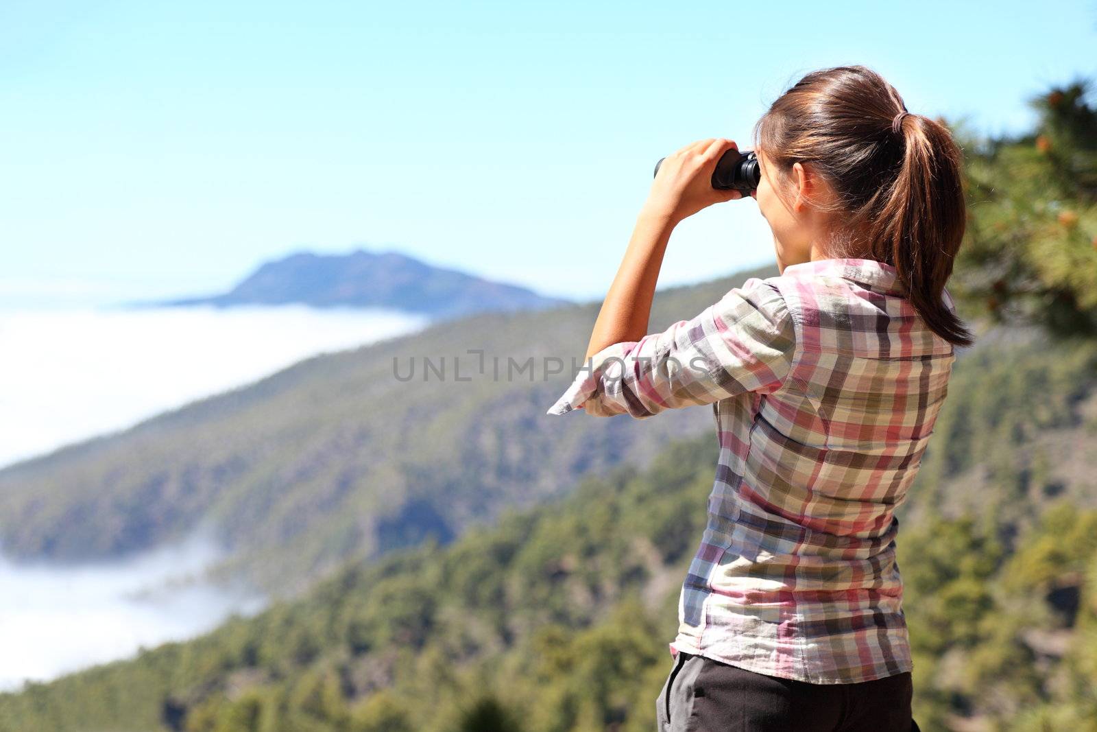Hiker looking in binoculars enjoying view above clouds during hiking trip. Young Asian woman on hike on La Palma, Canary Islands, Spain.
