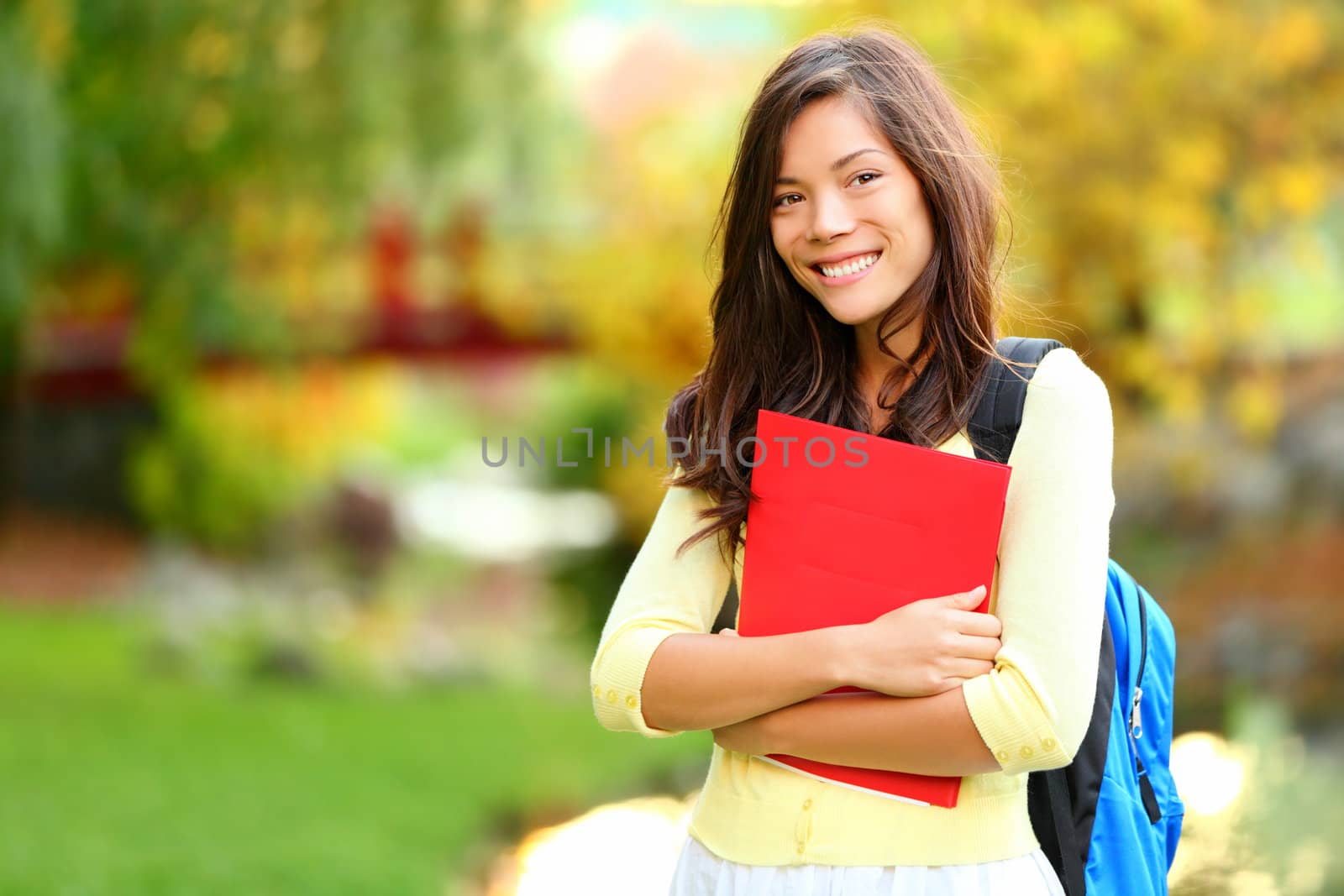 Beautiful woman holding red book in autumn background. Asian student girl on campus