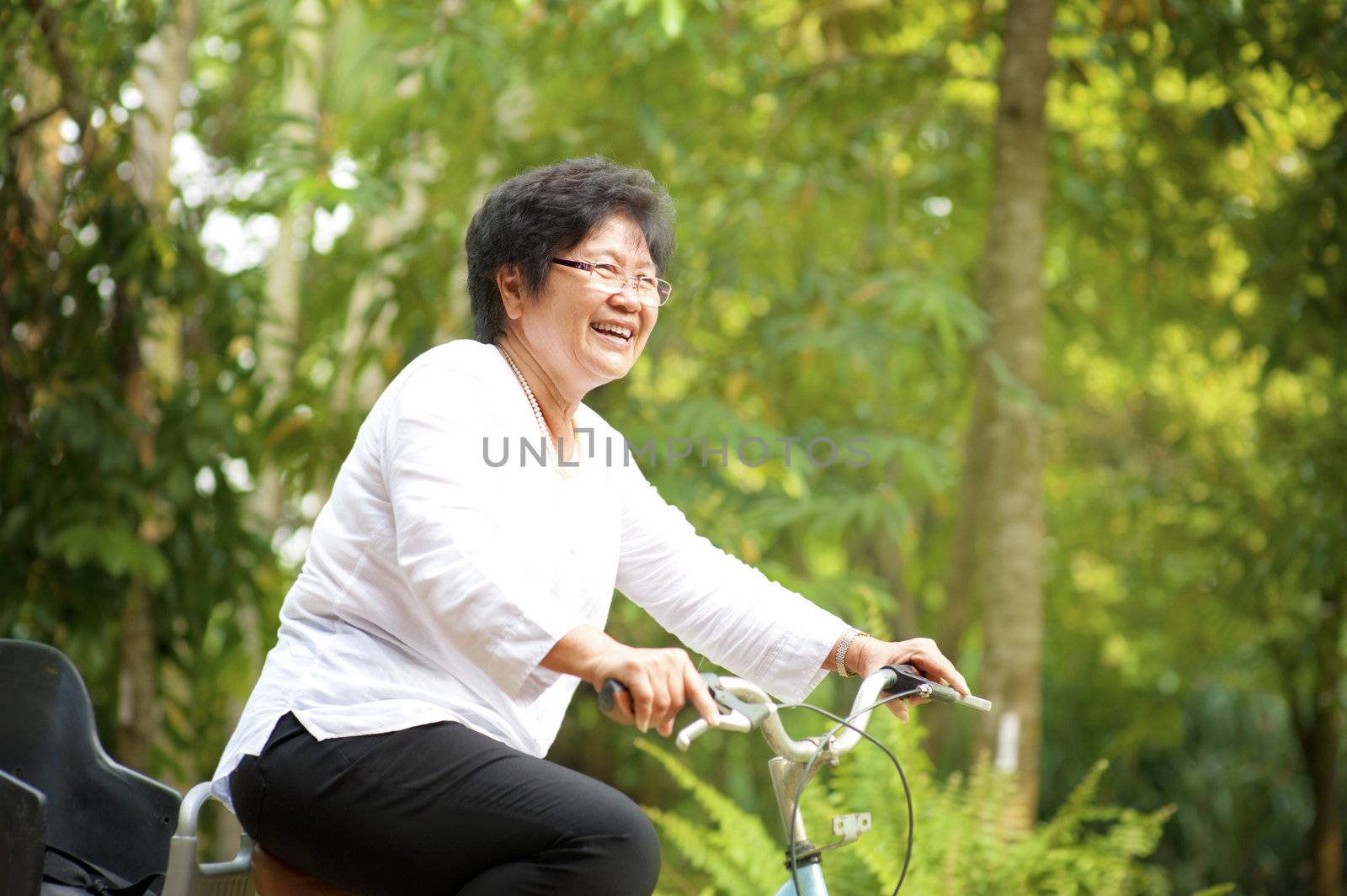60s senior Asian woman riding on bicycle outdoor with great fun
