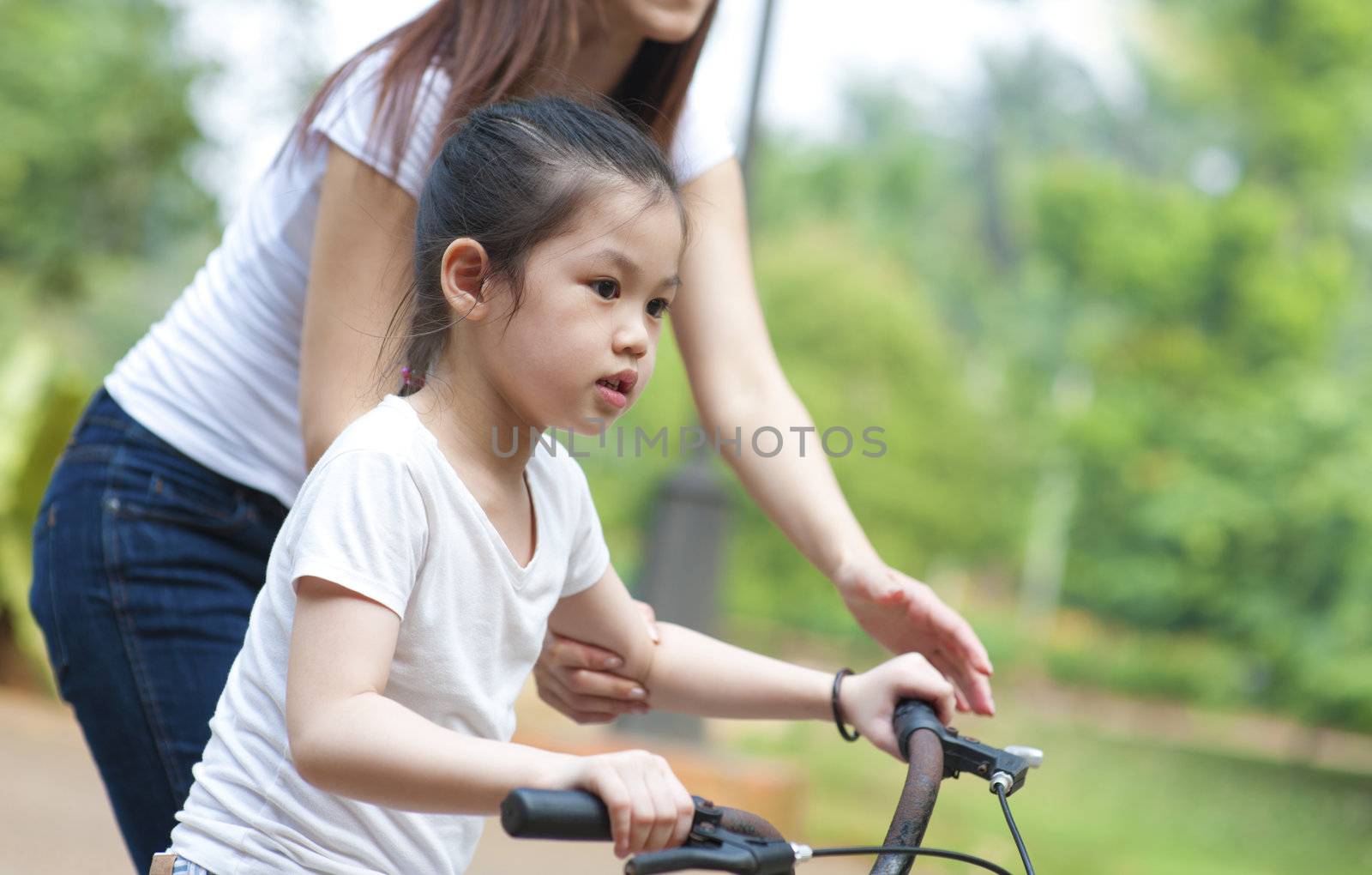 Asian Mother teaching daughter cycling at the park in the evening