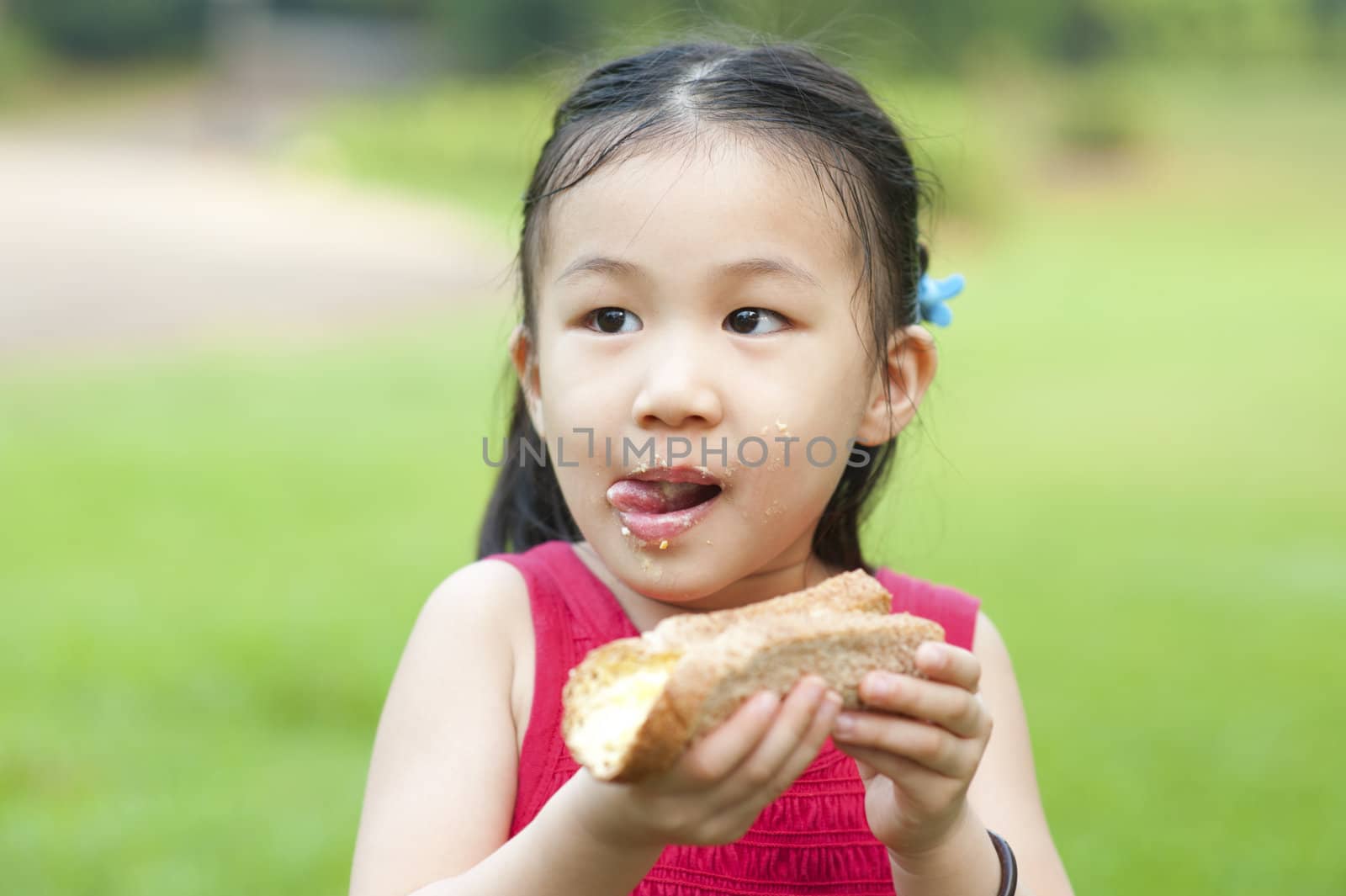 Little Asian girl eats a sandwich and licking lips on fresh air