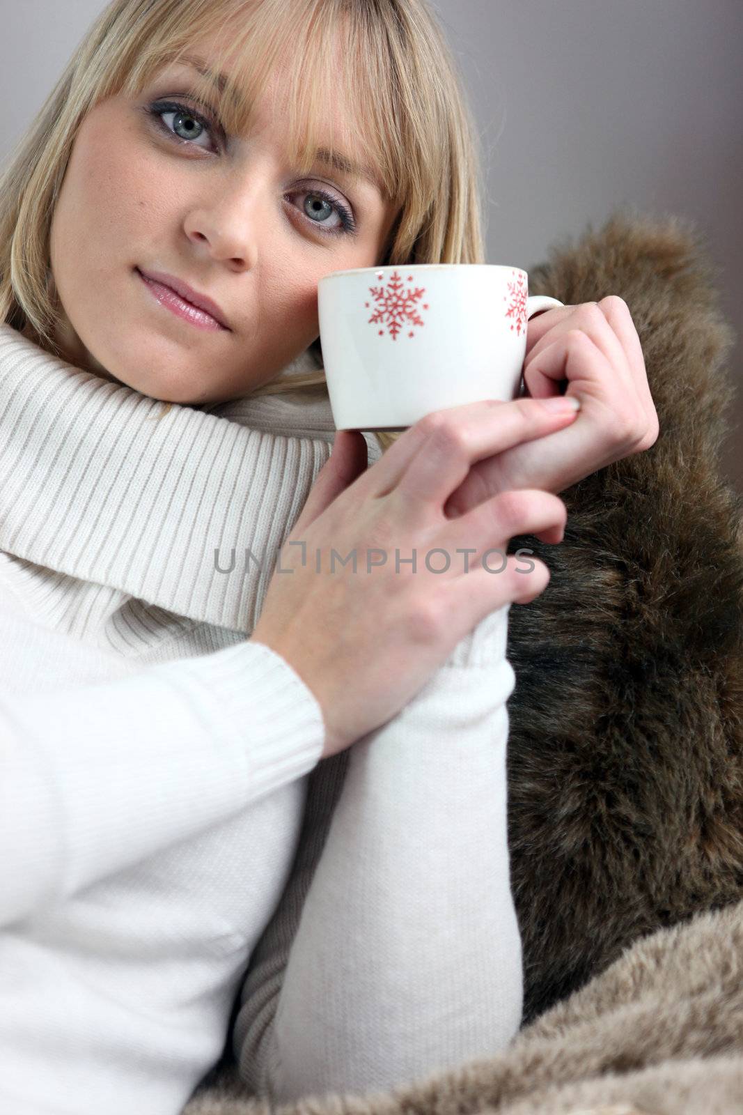 Woman sitting on cosy sofa with mug of coffee by phovoir