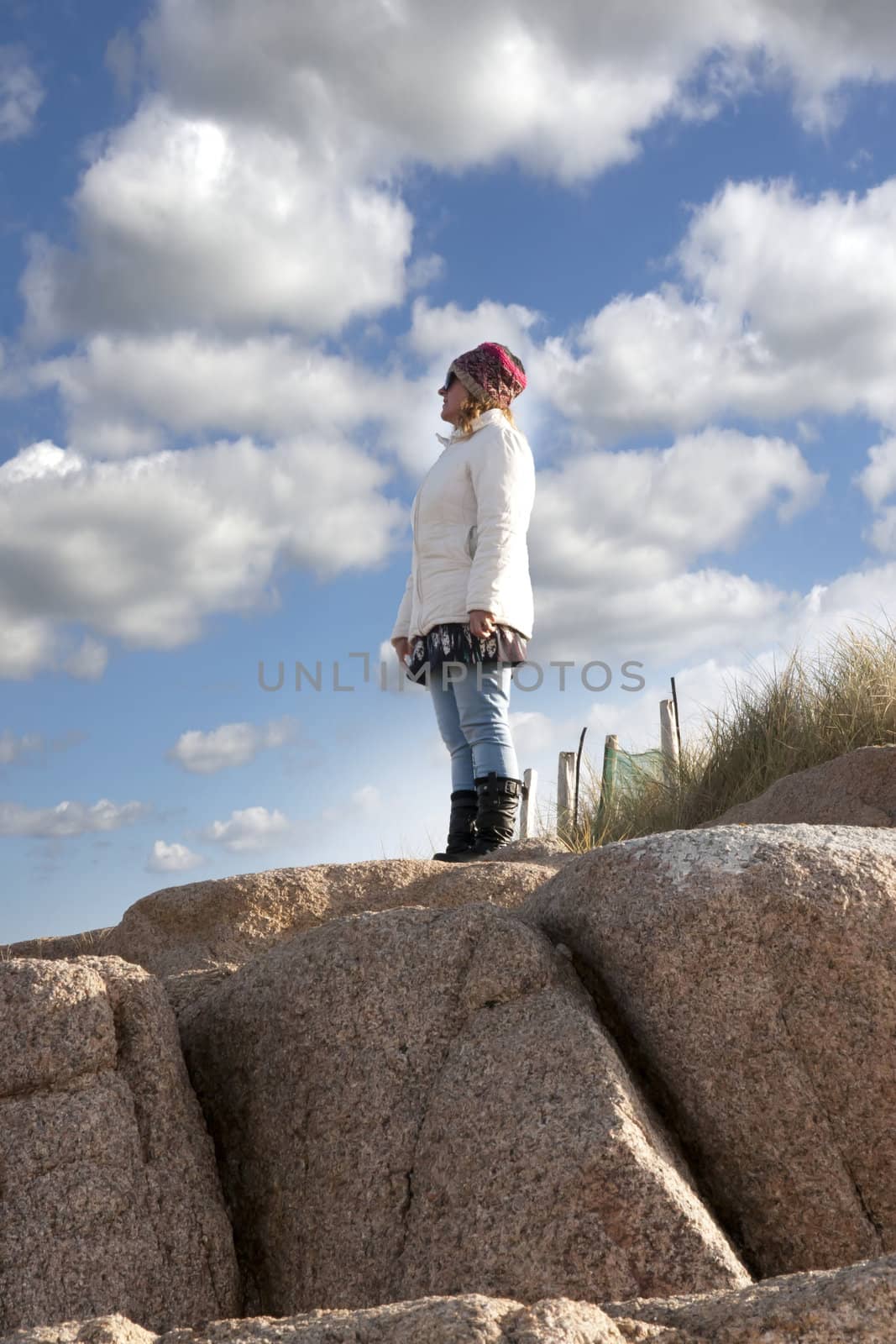 woman looking out to sea at the top of old natural rock formatio by morrbyte