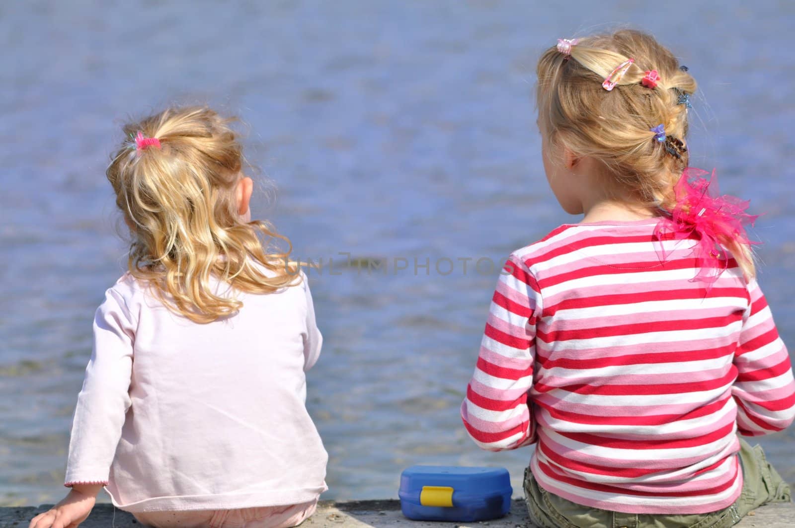 Two blond girls have a picnic on a lakefront