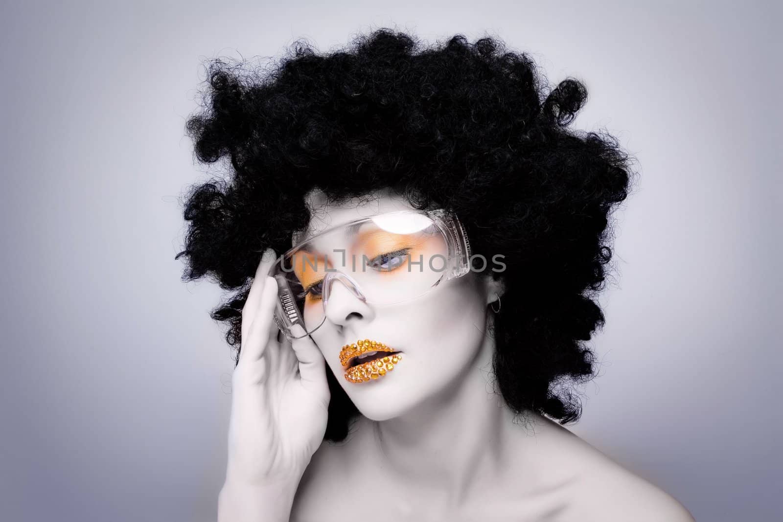 Young caucasian woman with gold fashion makeup and gold diamonties on her lips wearing a black afro wig