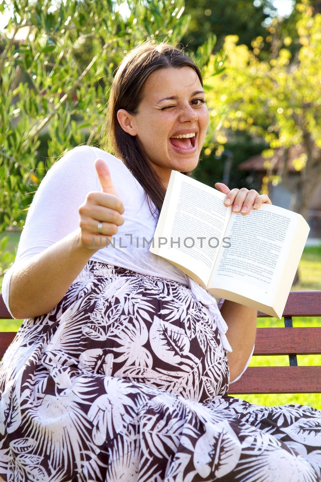 Happy pregnant woman with book thumb up by fmarsicano