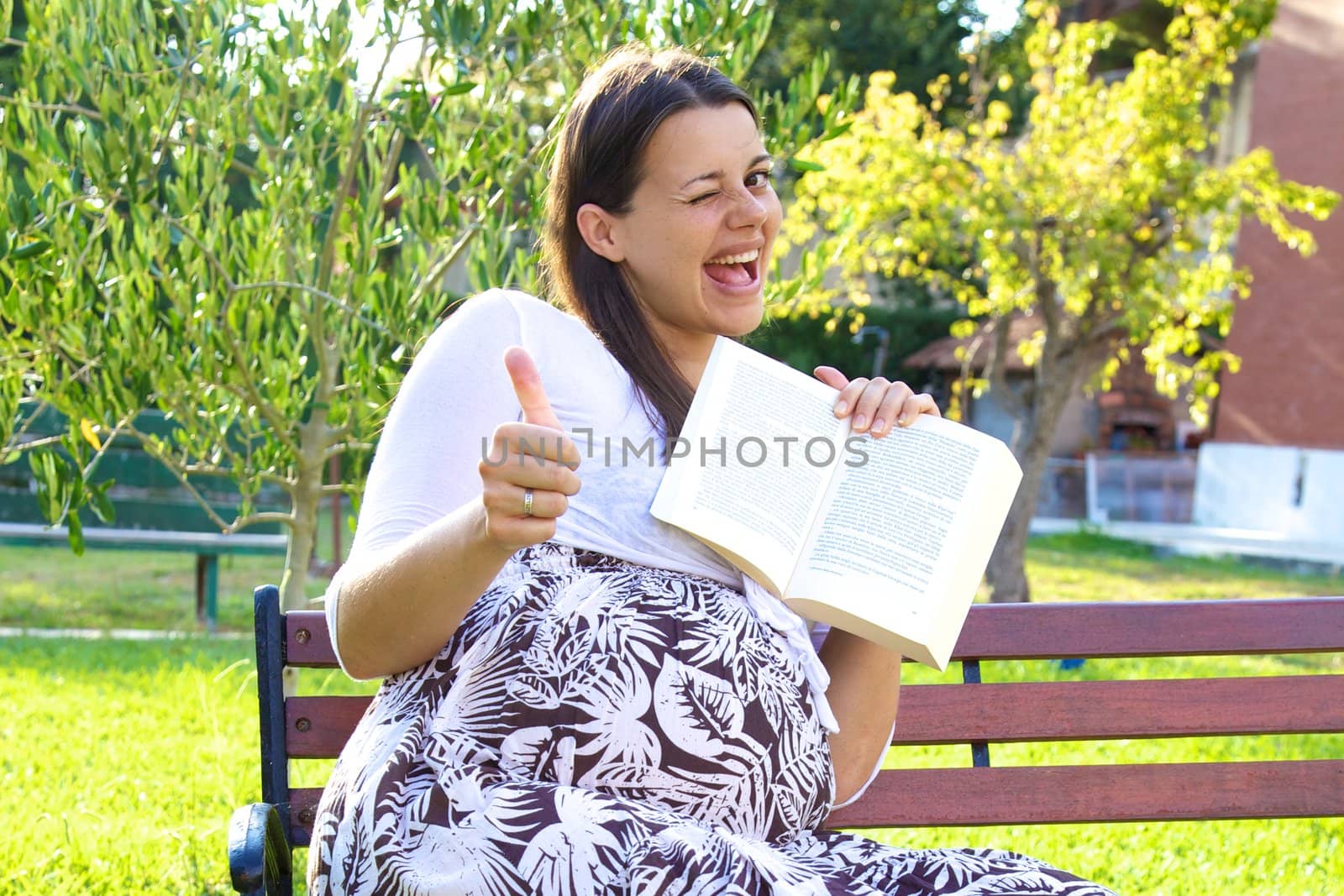 Happy female model pregnant showing book and thumb up