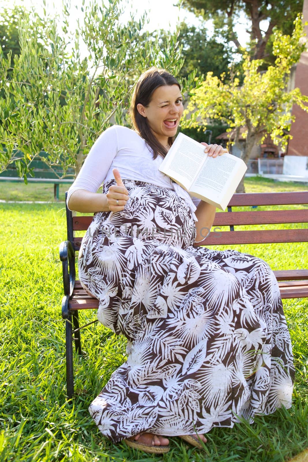 Beautiful pregnant young woman thumb up with book in hand