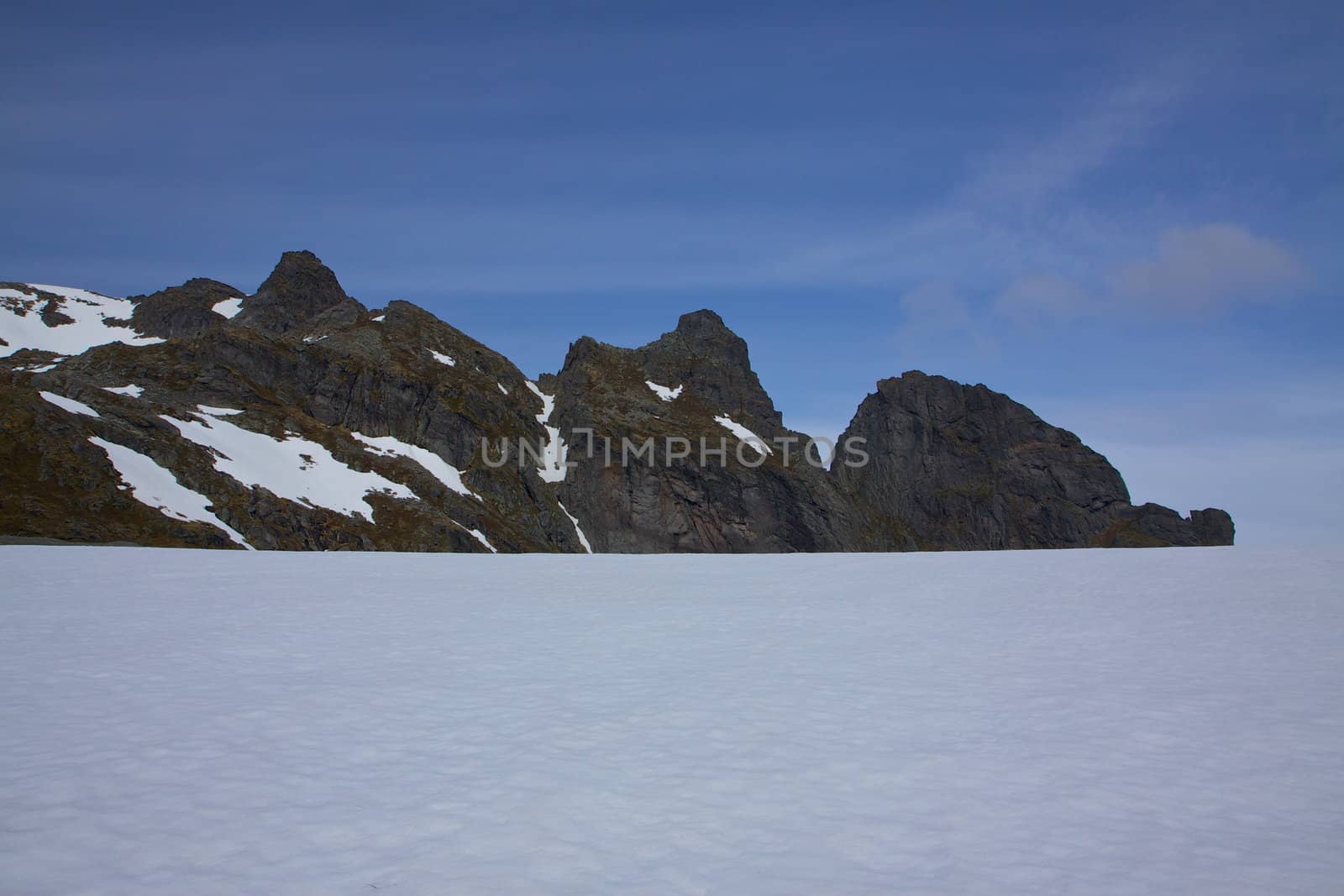Snow fields in the arctic Norway on Lofoten islands during summer with sharp mountain peaks towering above them