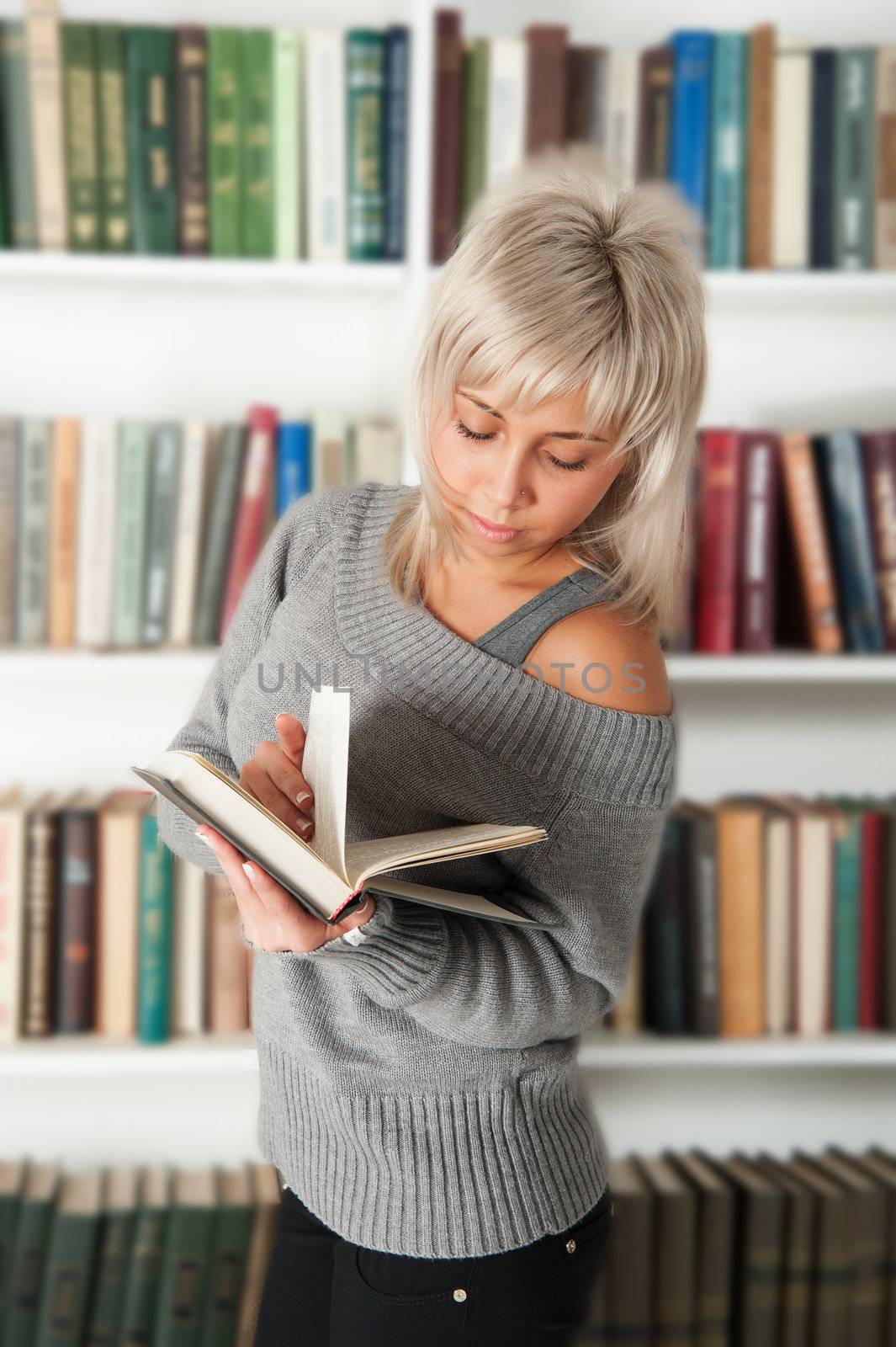 blonde holding a book in bookshelf