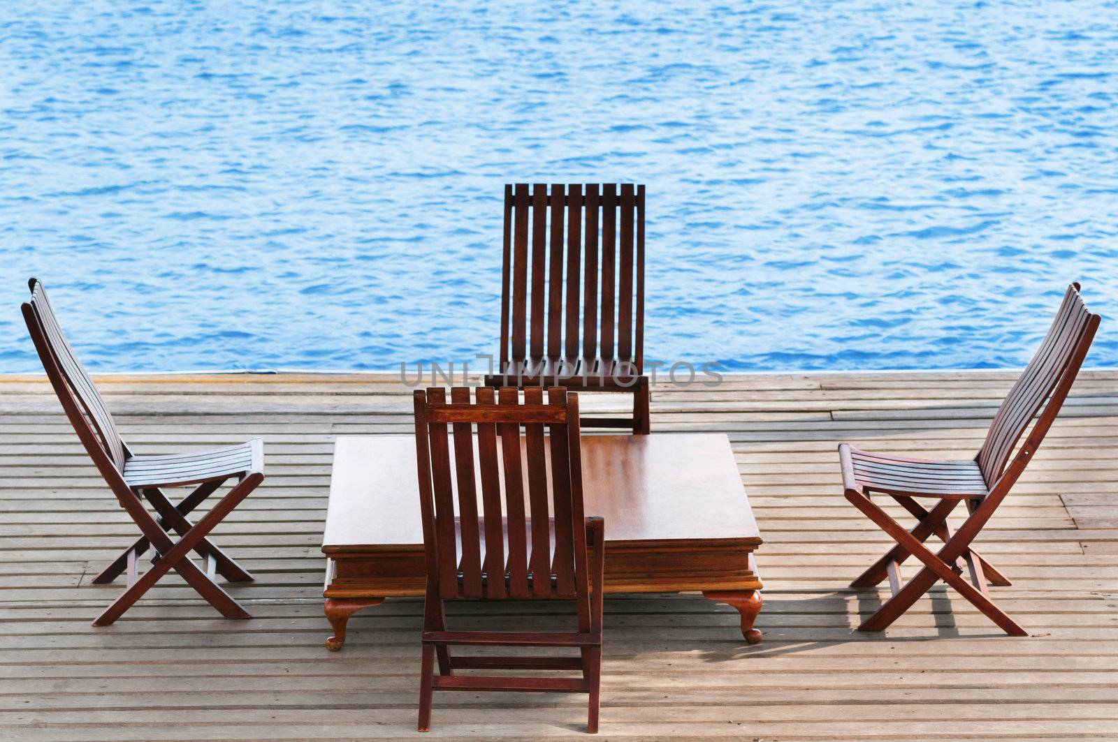 Wooden area with chairs and table on calm blue water