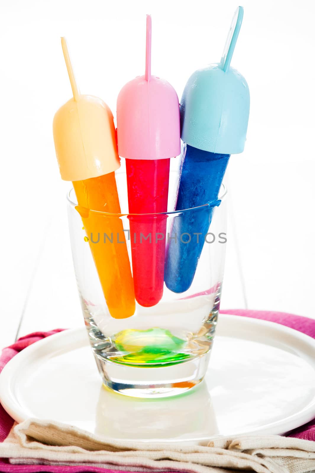 Yellow, red and blue Ice lolly in a glass on white background