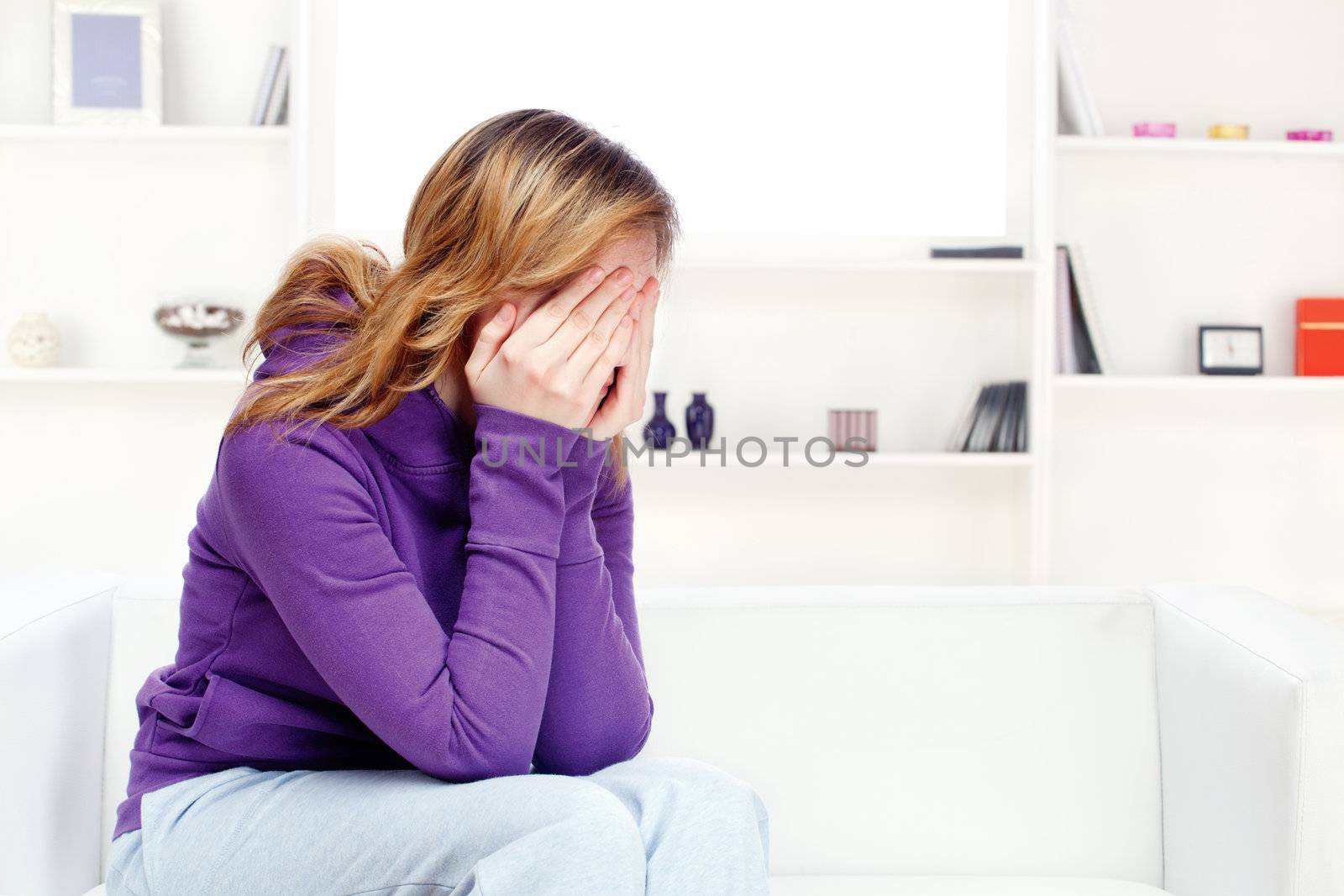 teenager girl at home seating on sofa and covering face with hands