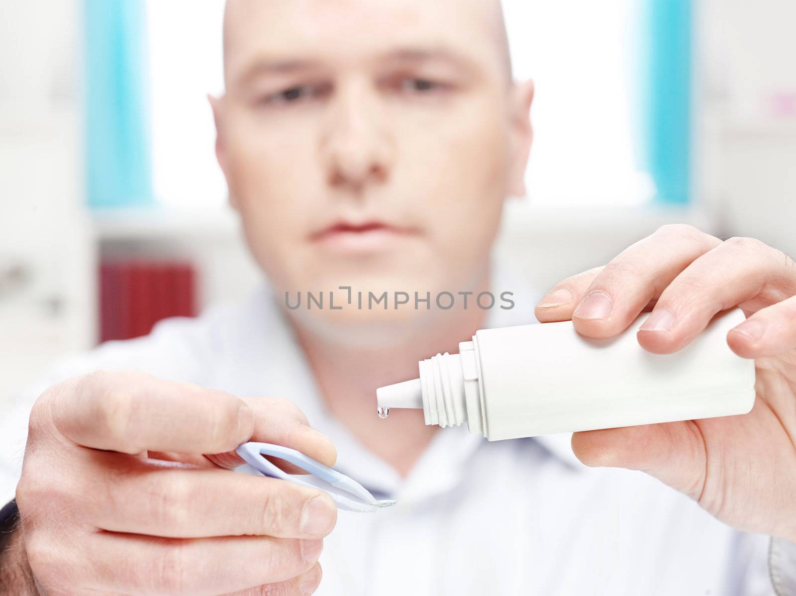 man clean contact lens at home, focus on drop of liquid from bottle