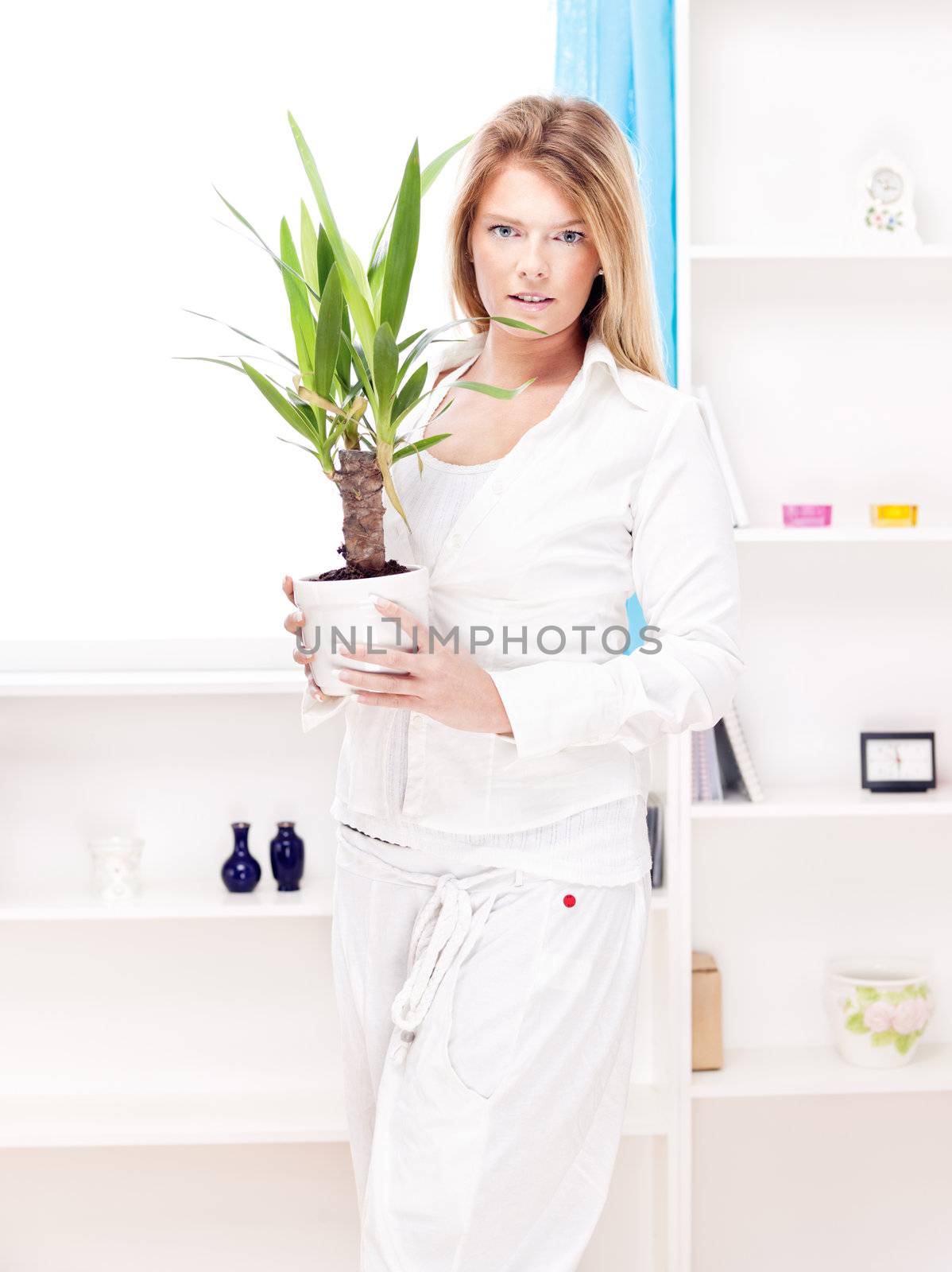Blond woman holding plant in pot at home