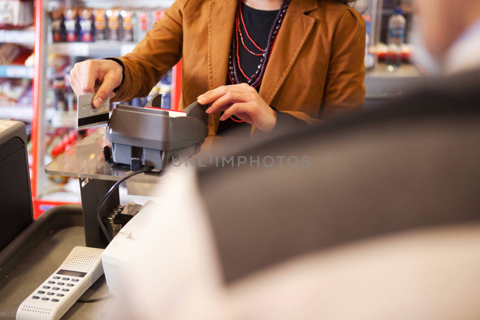 Shop assistant swiping credit card in supermarket with customer in the foreground