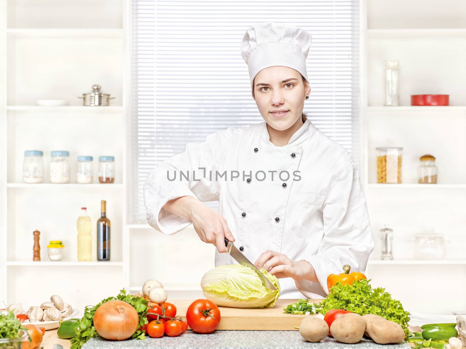 Young female chef cutting cabbage on the cutting board in kitchen