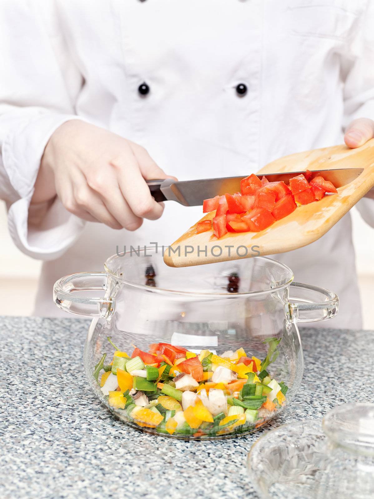 chef adds chopped tomatoes in a glass bowl with other vegetables