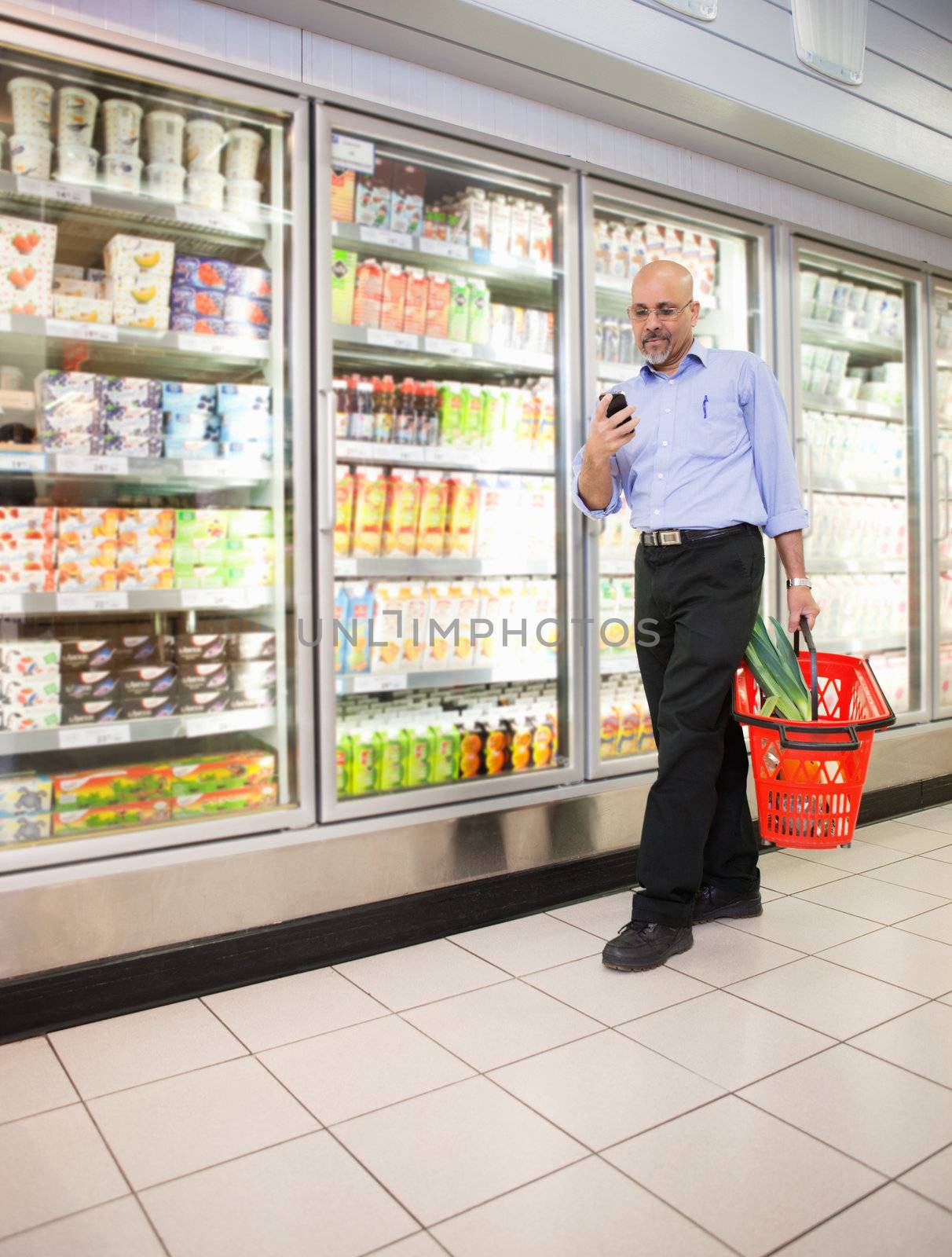 Mature man looking at mobile phone while walking in front of refrigerators in shopping centre